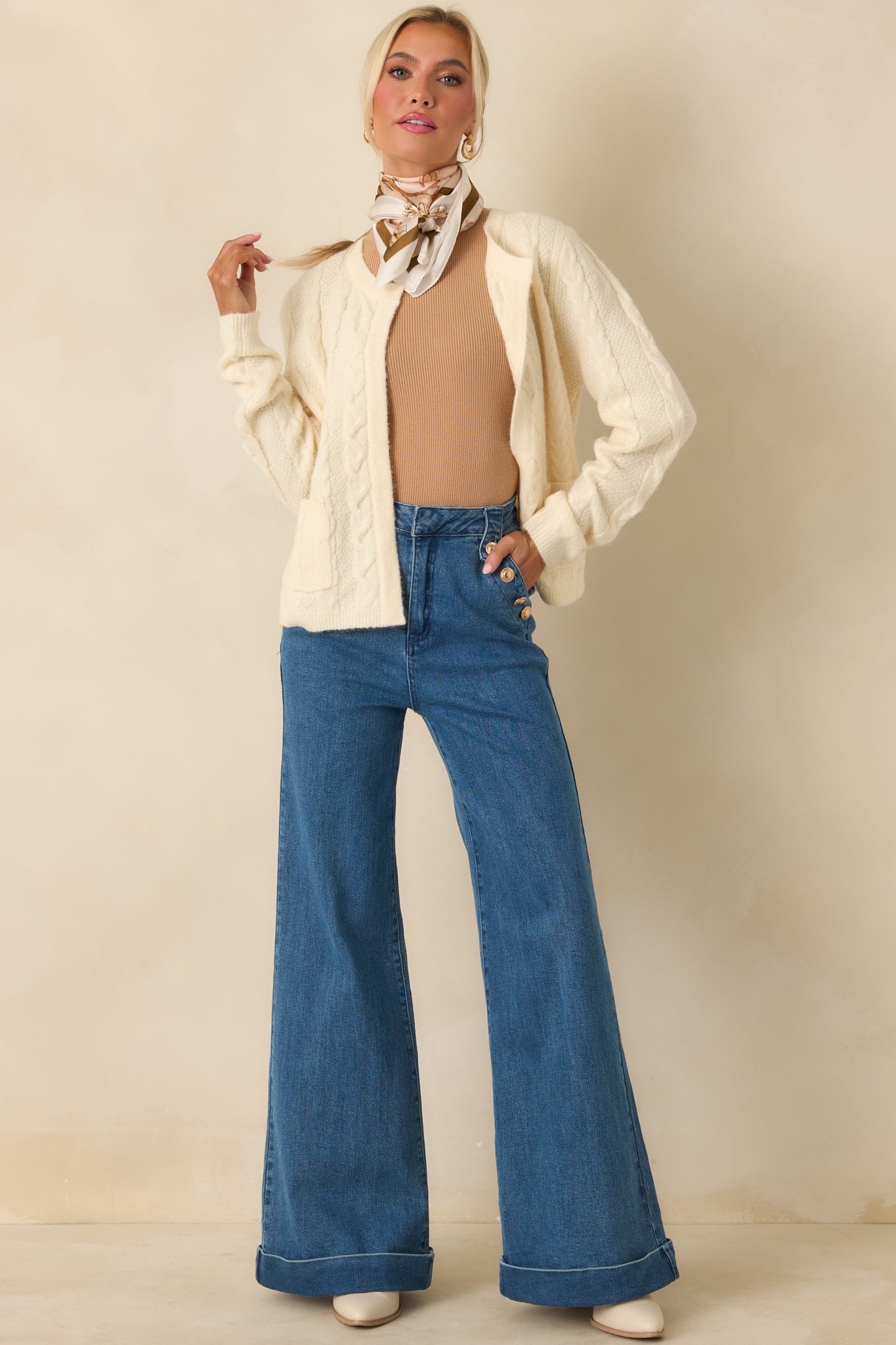 Soft ivory knit cardigan featuring classic cable pattern, relaxed fit, and long sleeves for layered everyday wear.