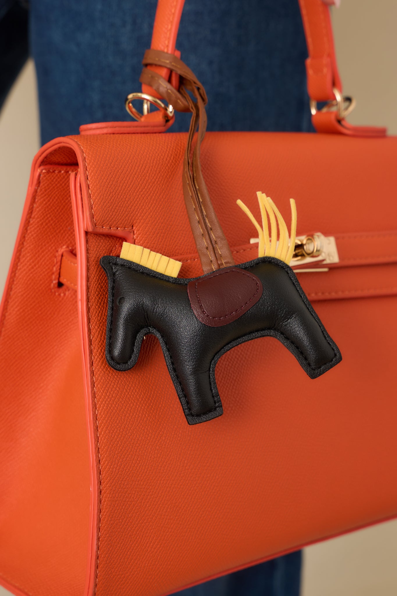 Close-up of orange handbag showing the twist lock closure, overlapping flap straps, and smooth faux leather texture.