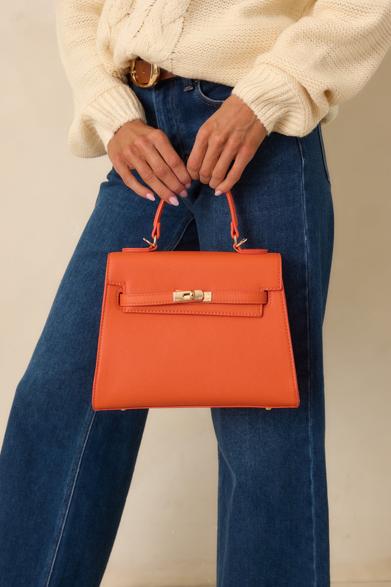 Cropped detail highlighting structured silhouette, top handle, and removable shoulder strap of the orange faux leather handbag.