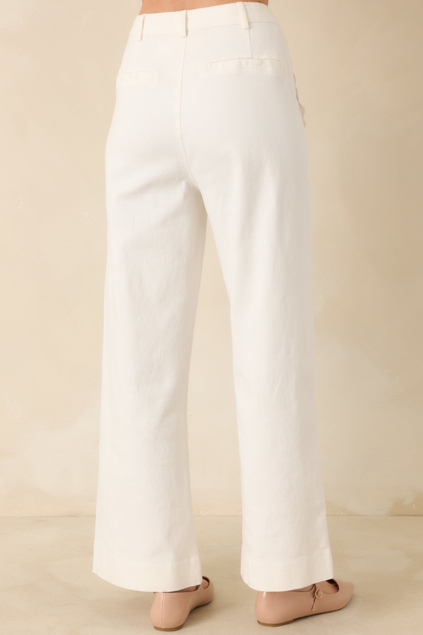 Back view of ivory high-rise pants featuring welt pockets and wide leg silhouette.