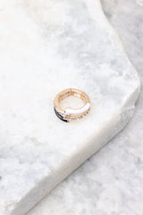 Overhead marble shot of ring that features gold hardware, black and white accents, rhinestone detailing, and elastic under the band measuring 0.75