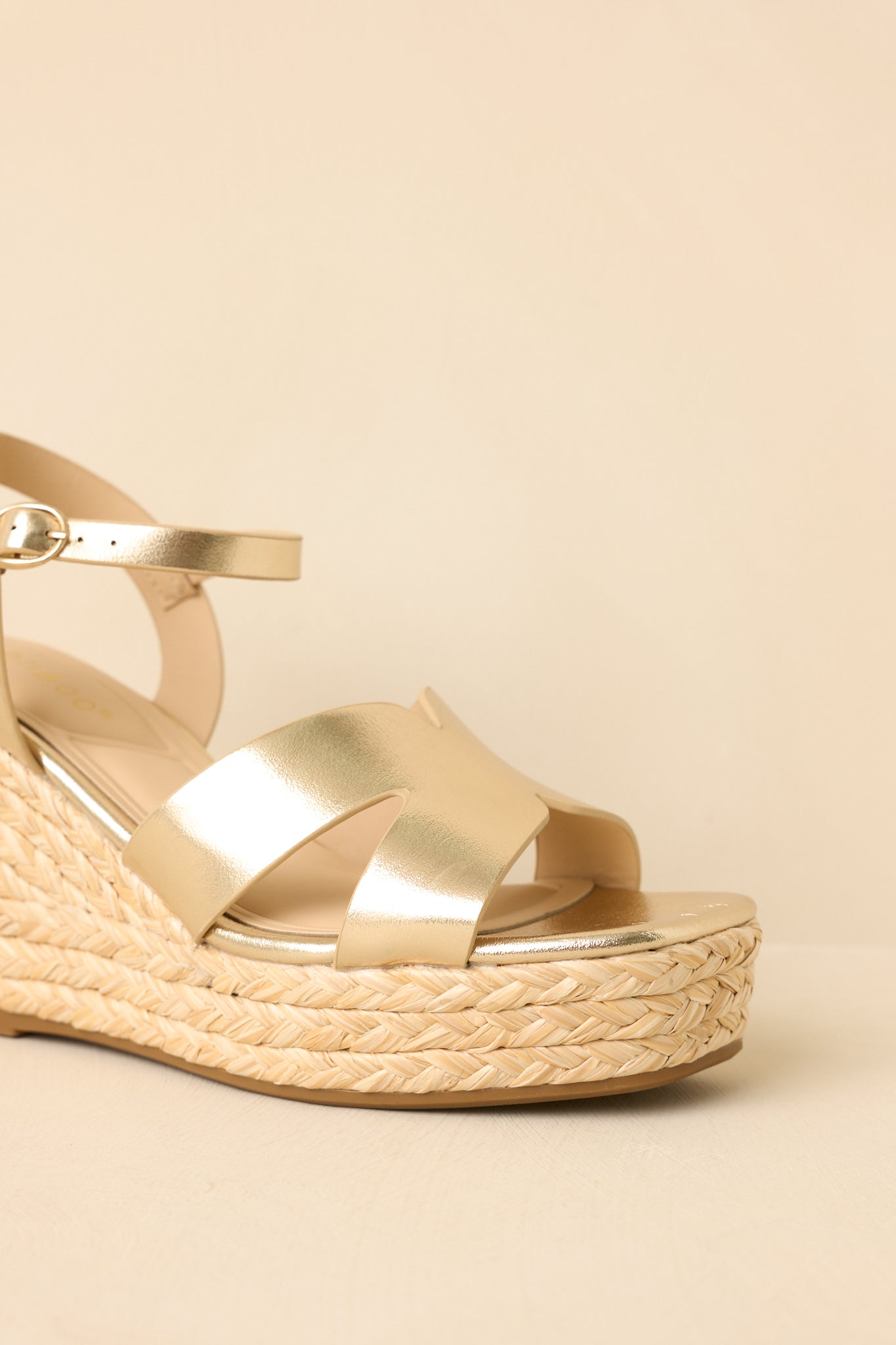Front view of wedge sandals on a beige background emphasizing the cut-out gold straps and cushioned footbed.