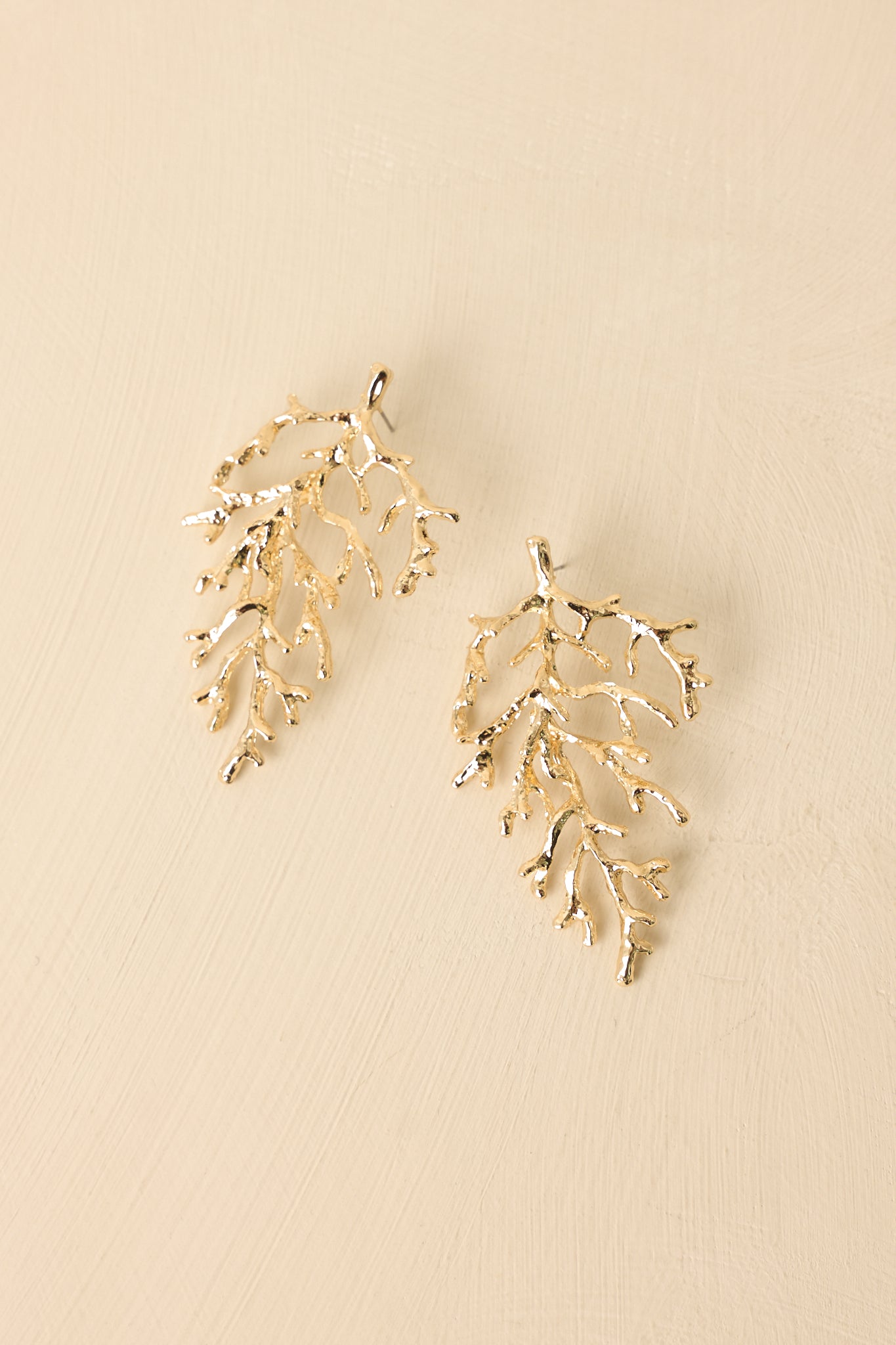 Front view of gold coral drop earrings displayed on beige background emphasizing sculptural organic form.