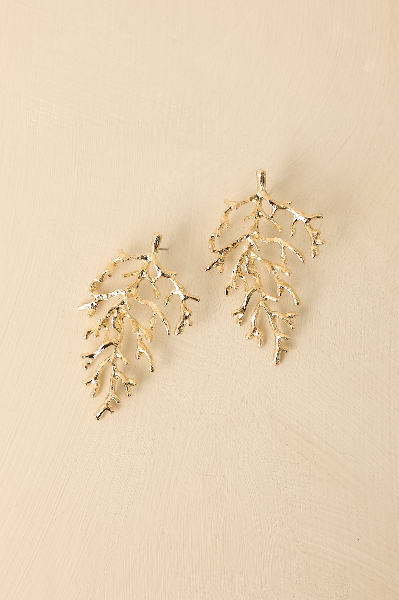 Angled view of textured coral-inspired earrings on beige backdrop highlighting depth and shine.