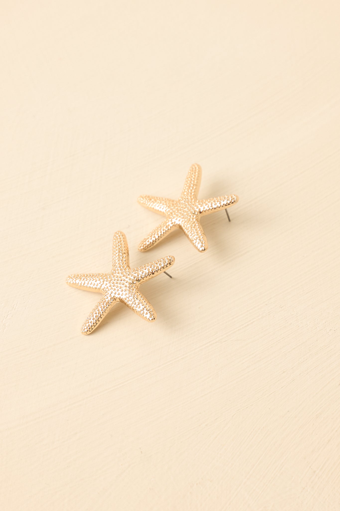 Angled view of starfish-inspired drop earrings on beige backdrop highlighting depth and shine.