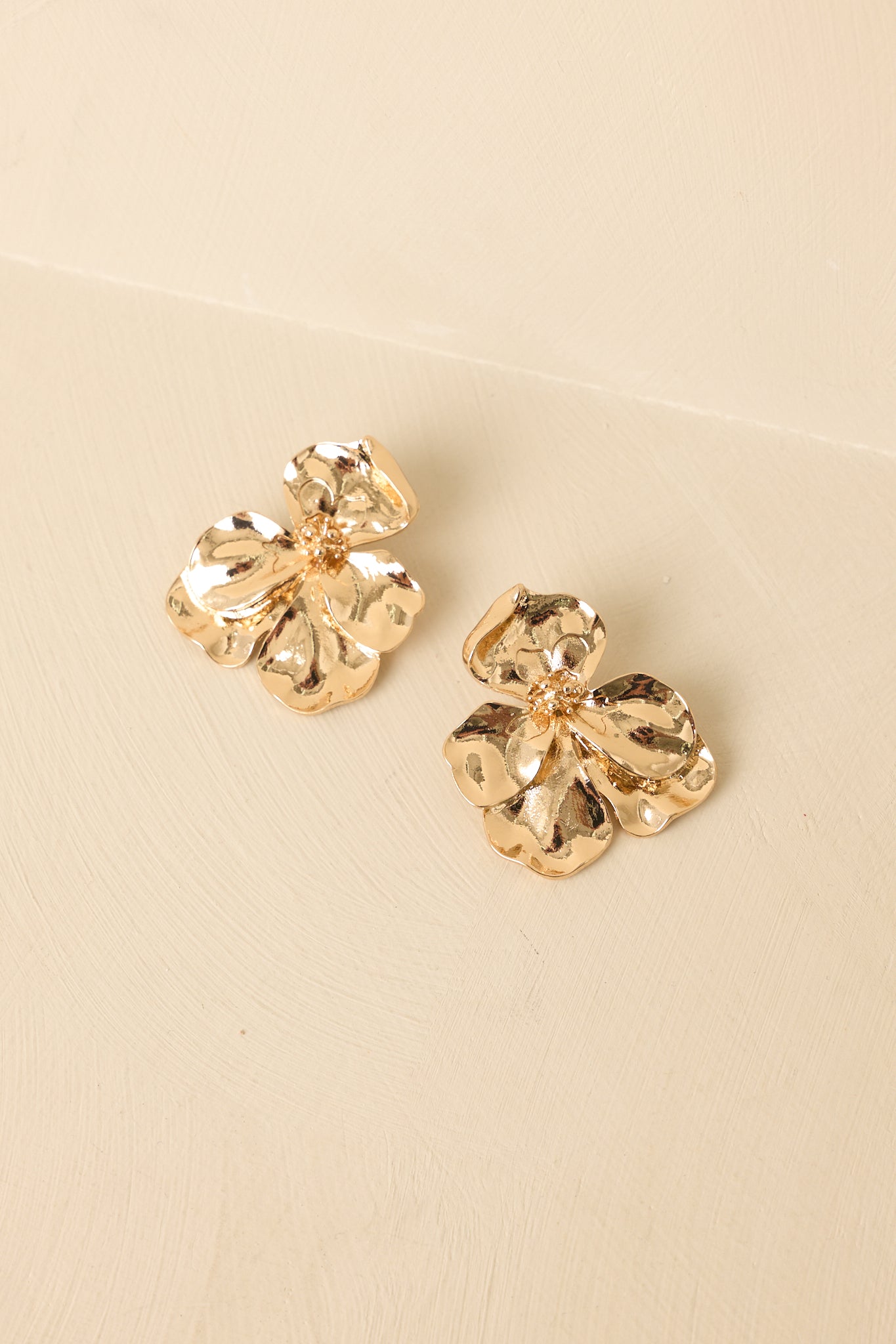 Detailed close-up of gold floral earrings showcasing hammered petal texture and dimensional center design.