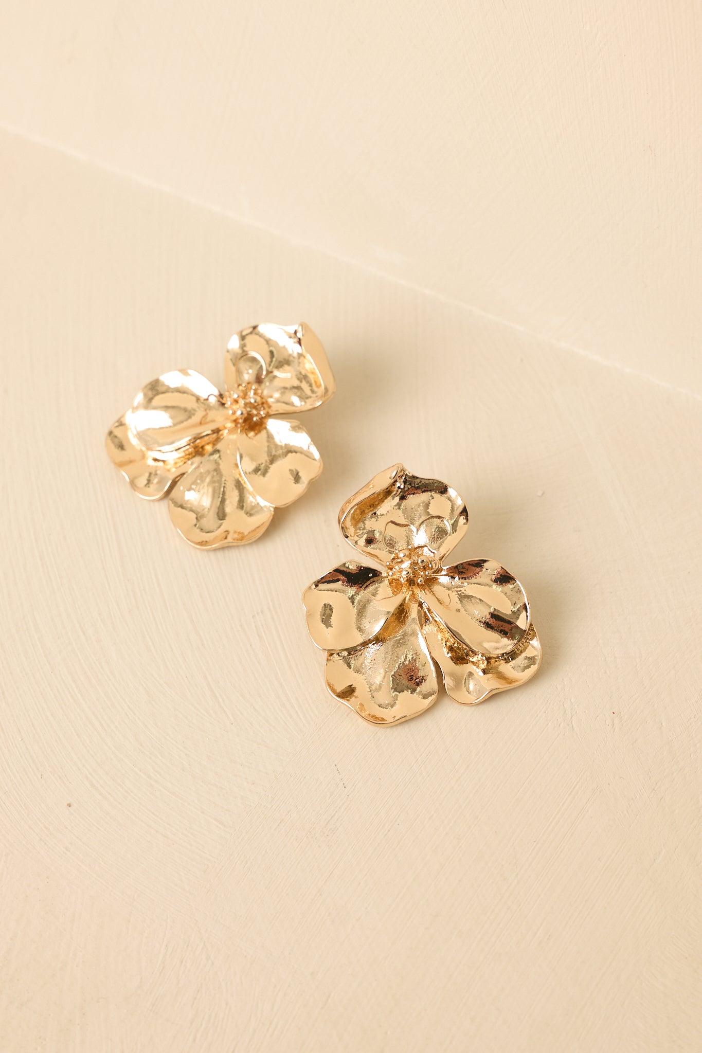 Angled view of gold statement earrings on a beige background highlighting sculptural bloom shape and radiant finish.
