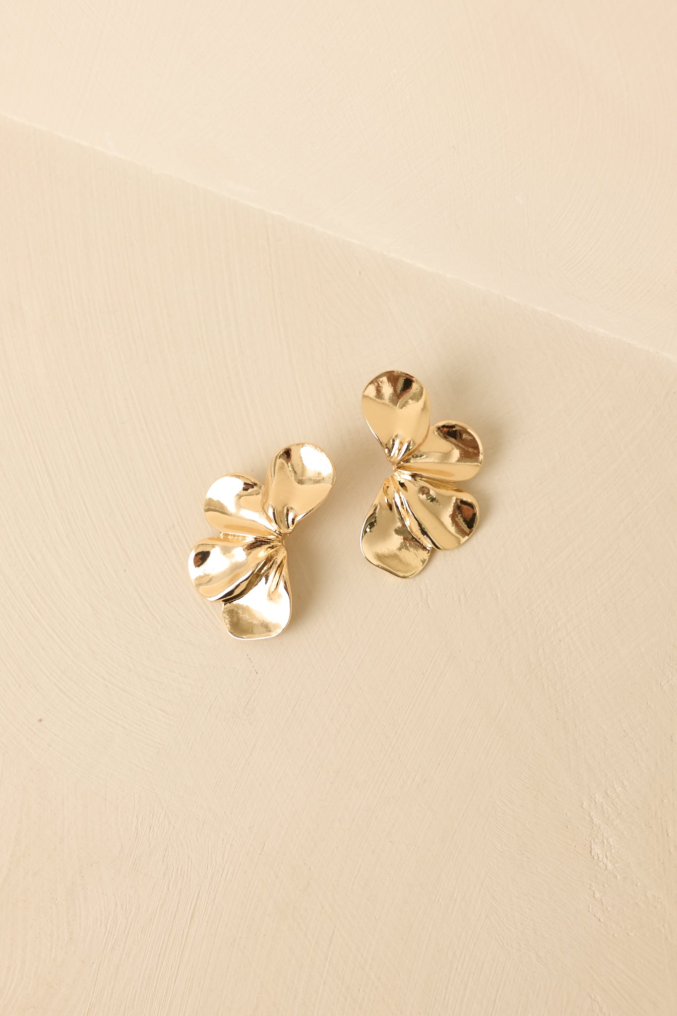 Angled view of sculpted floral earrings on beige backdrop highlighting shine and depth.
