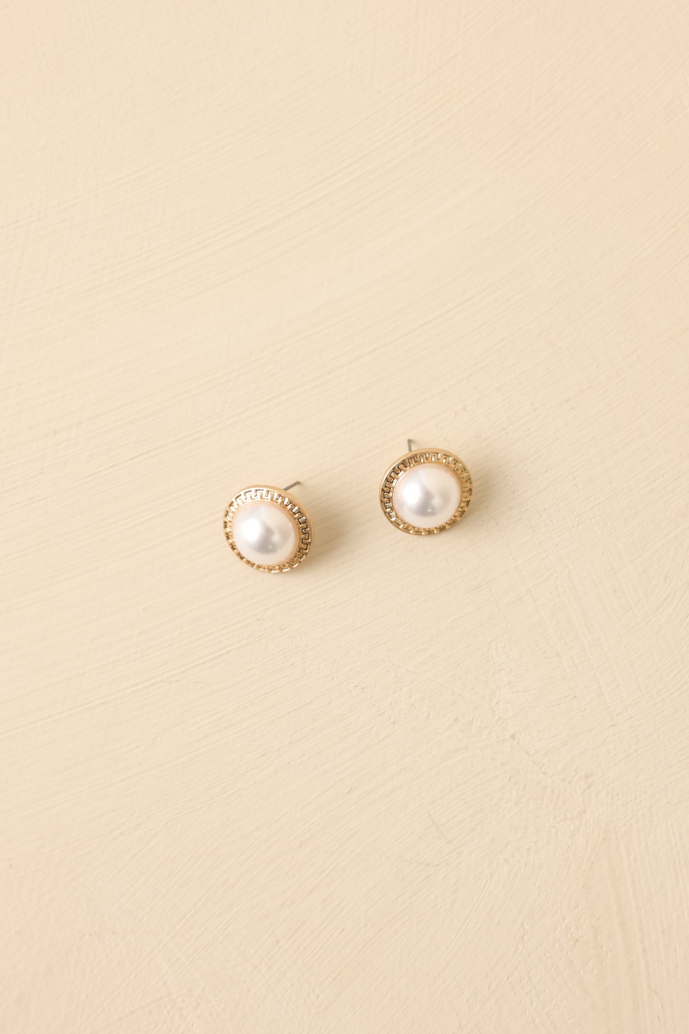 Angled view of gold and pearl studs on beige backdrop emphasizing refined texture and shine.