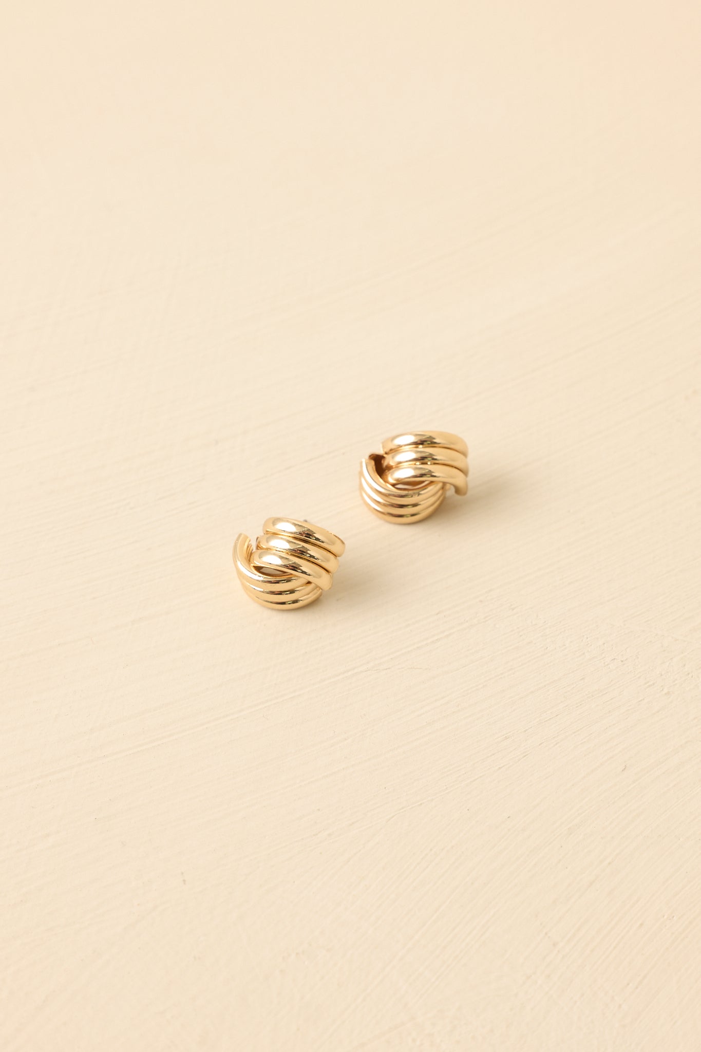 Close-up detail of gold earrings showing sculpted knot shape and secure post-back closure.