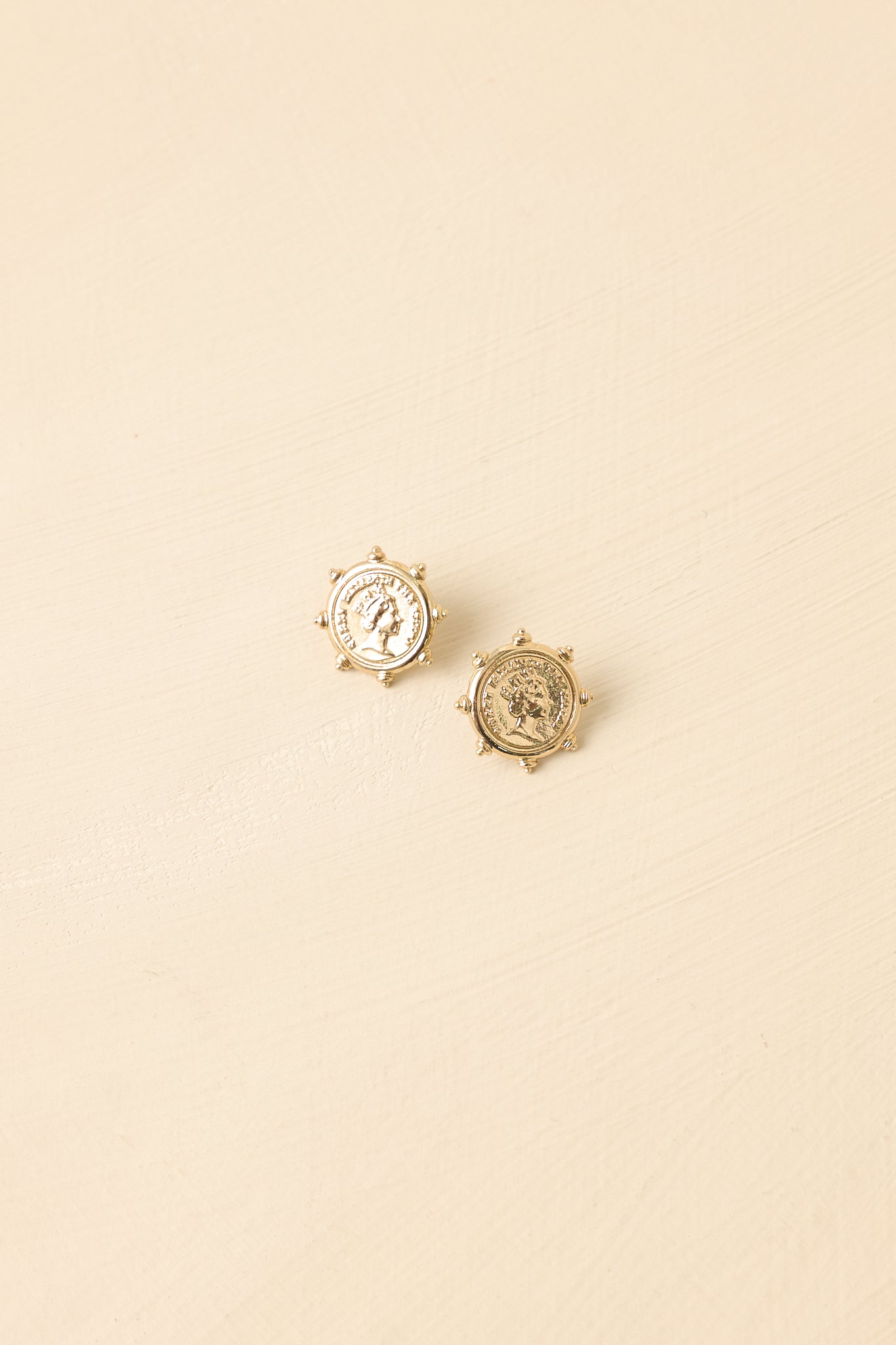 Front view of gold coin earrings displayed on beige background emphasizing embossed design and beaded edges.