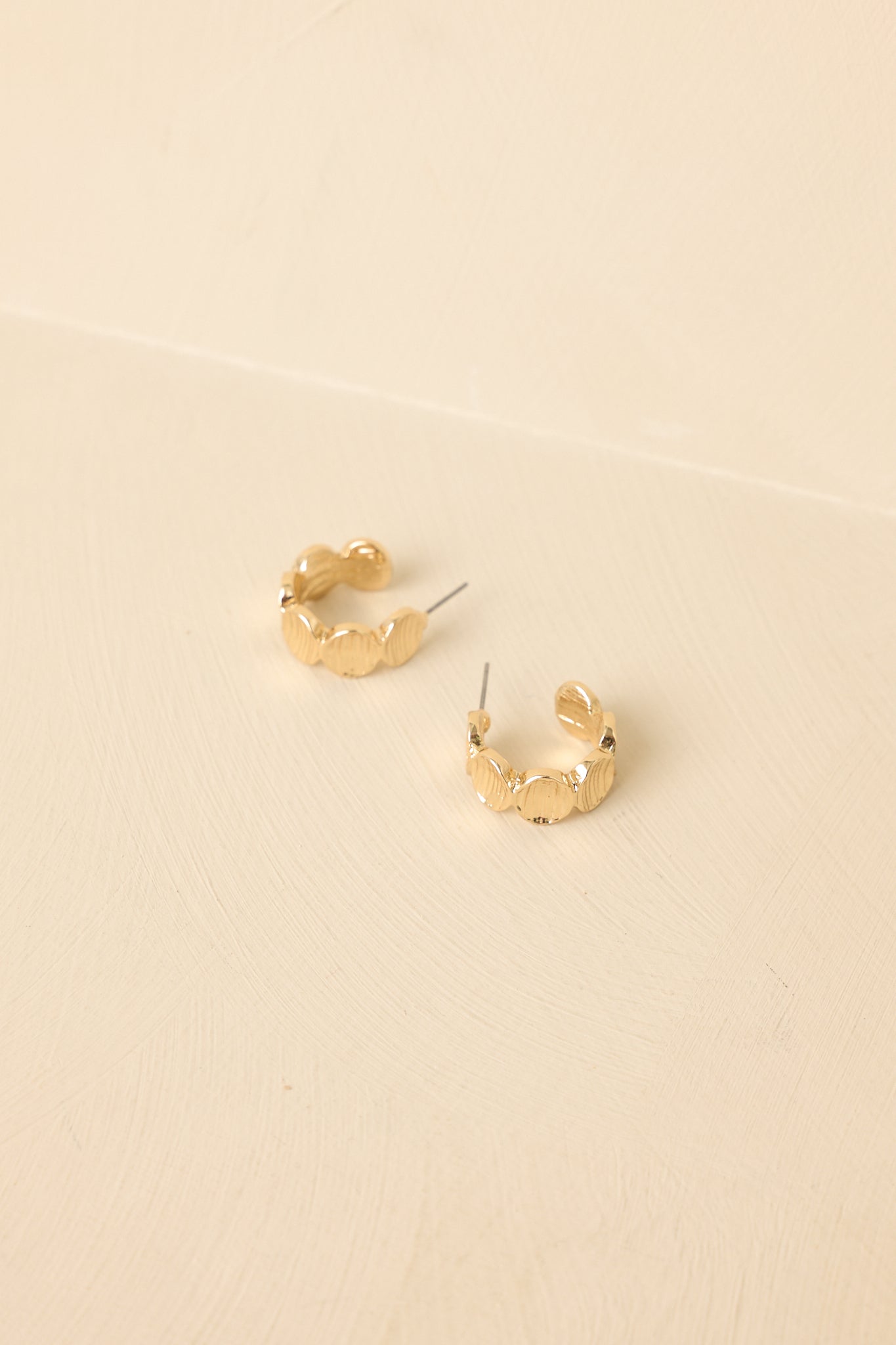 Angled view of segmented hoop earrings on beige backdrop highlighting dimensional shape and shine.