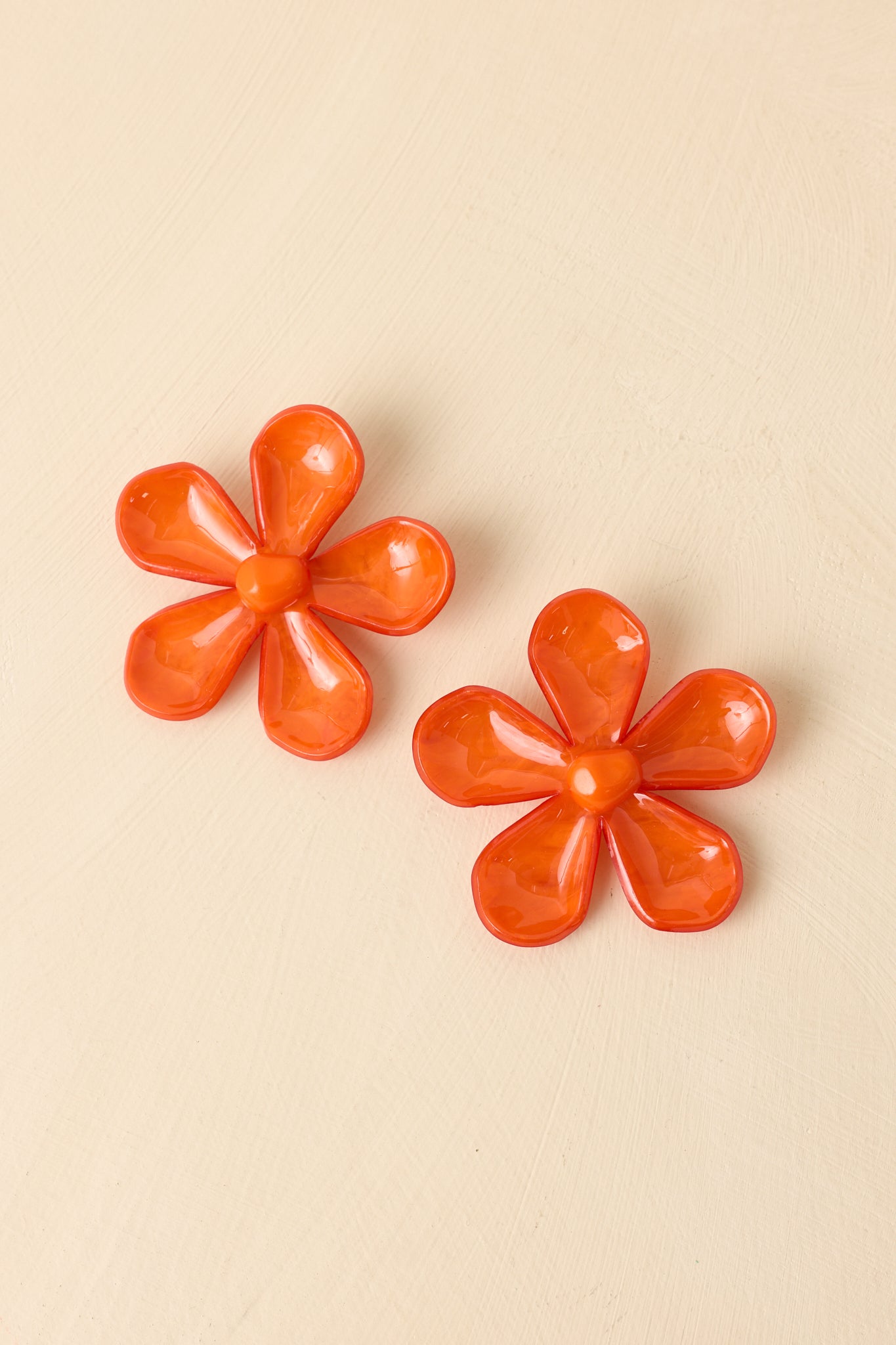 Close-up detail of orange earrings showing sculpted petals, glossy finish, and statement silhouette.