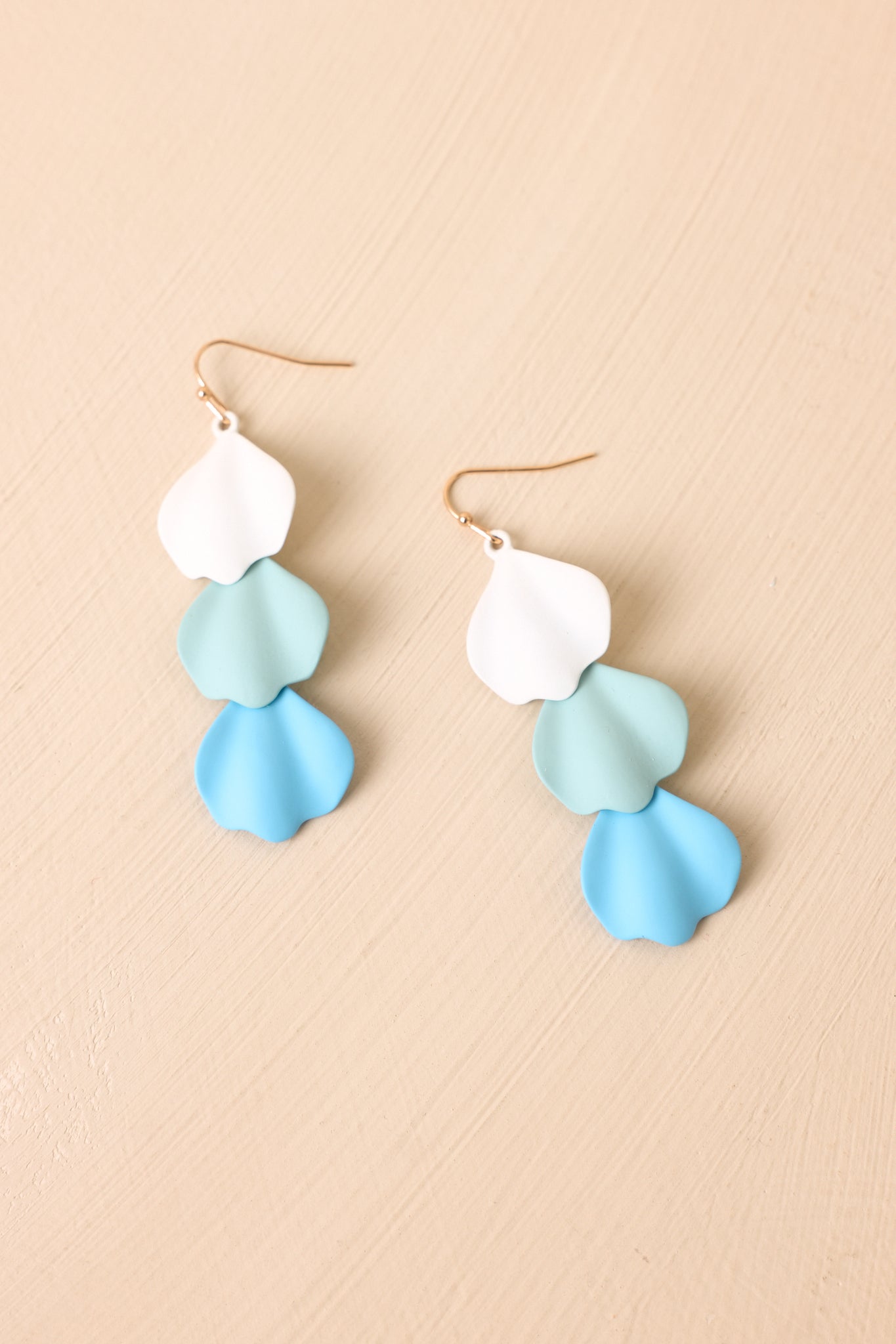 Angled view of blue earrings on a beige background highlighting overlapping petal shapes and soft modern structure.