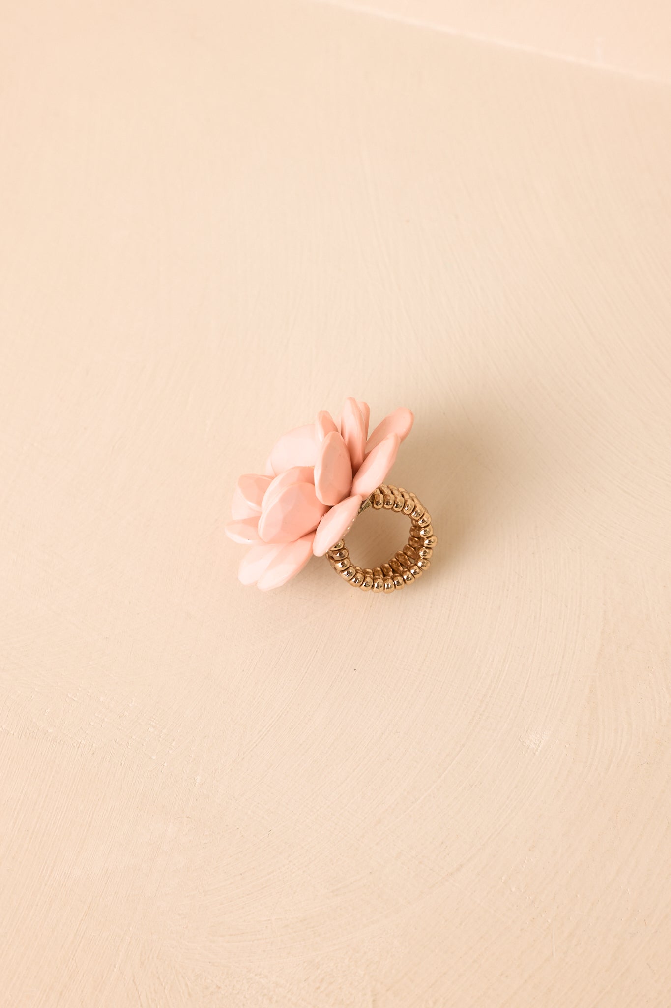 Pink floral statement ring displayed on a beige background showcasing its soft petal layers and polished glossy surface.
