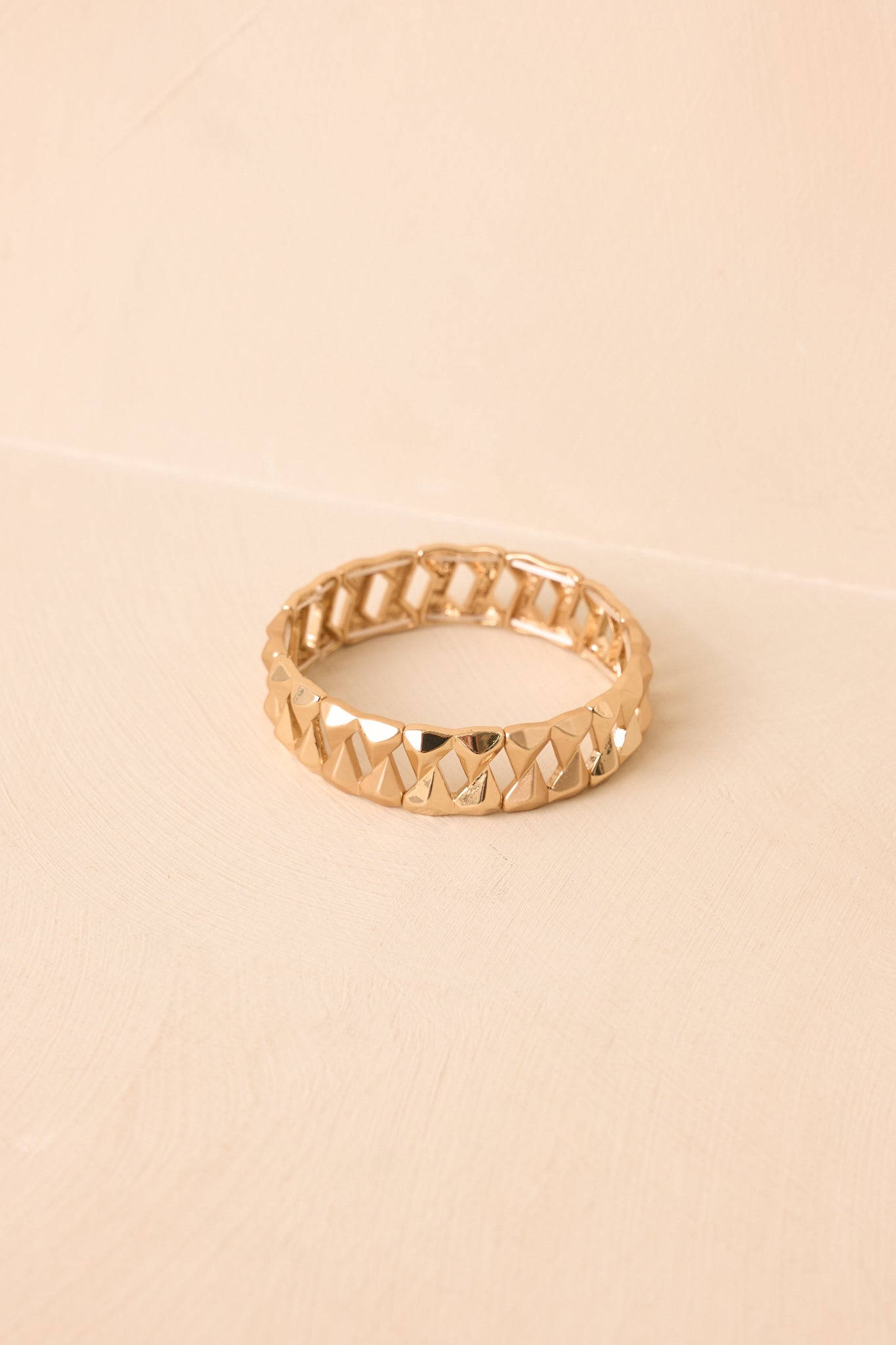 Gold geometric link bracelet displayed on a beige background showcasing its textured faceted surface and modern chunky shape.