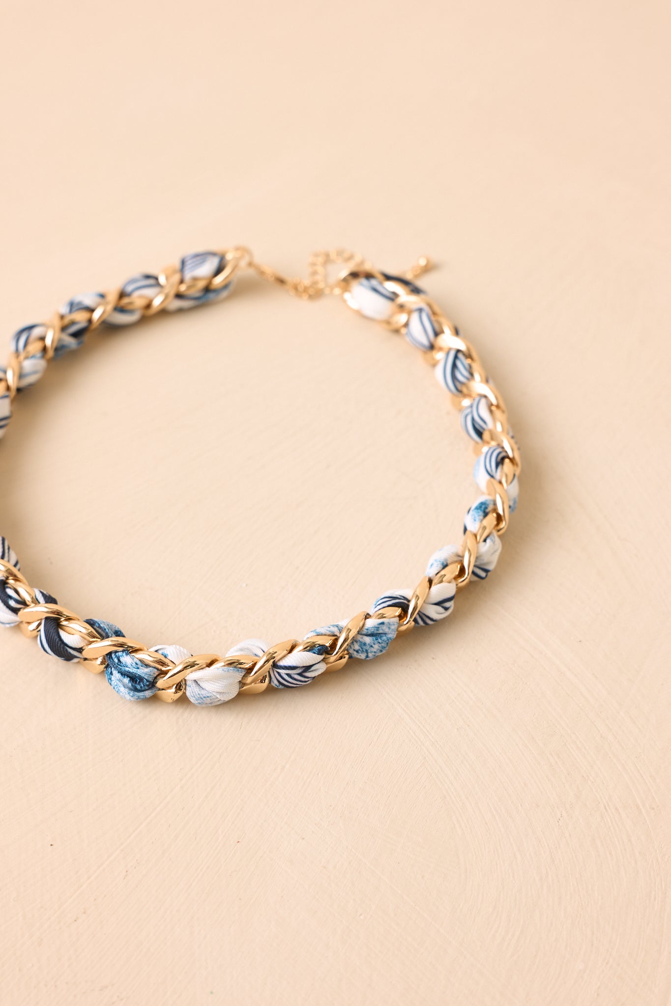 Angled view of woven chain necklace on beige backdrop emphasizing layered texture and bold design.