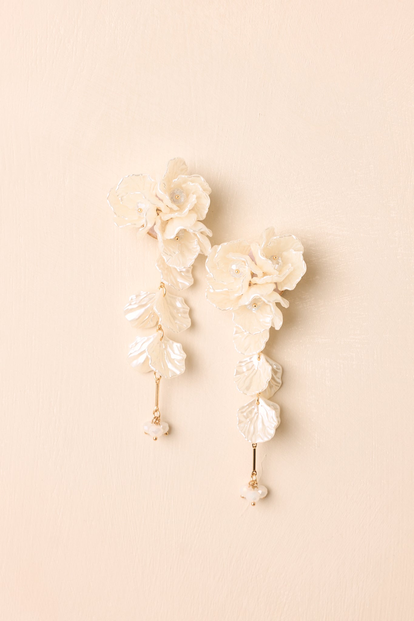 Front view of ivory floral drop earrings displayed on beige background emphasizing sculpted petals.