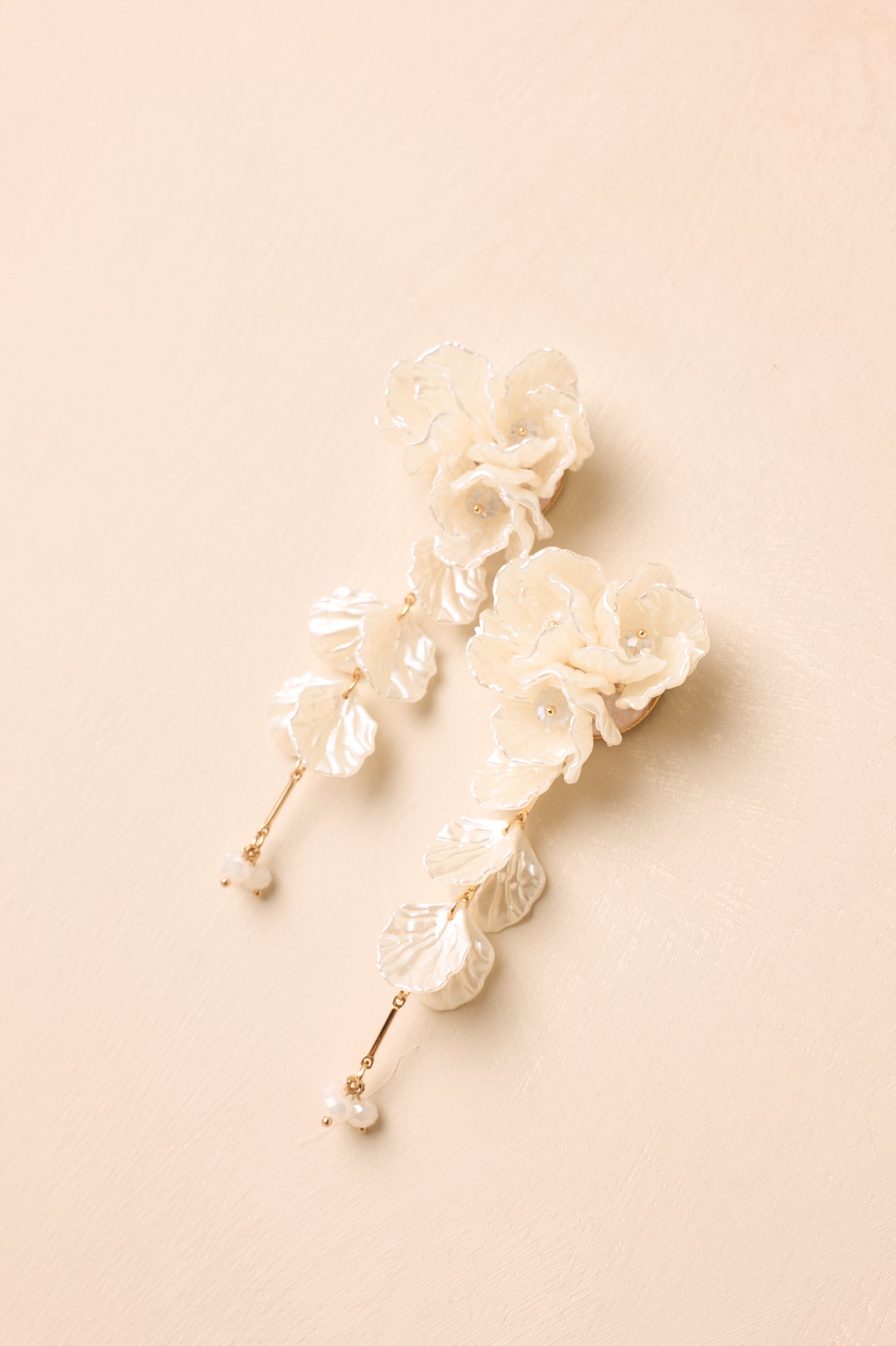 Angled view of cascading floral earrings on beige backdrop highlighting dimension and soft ivory tone.