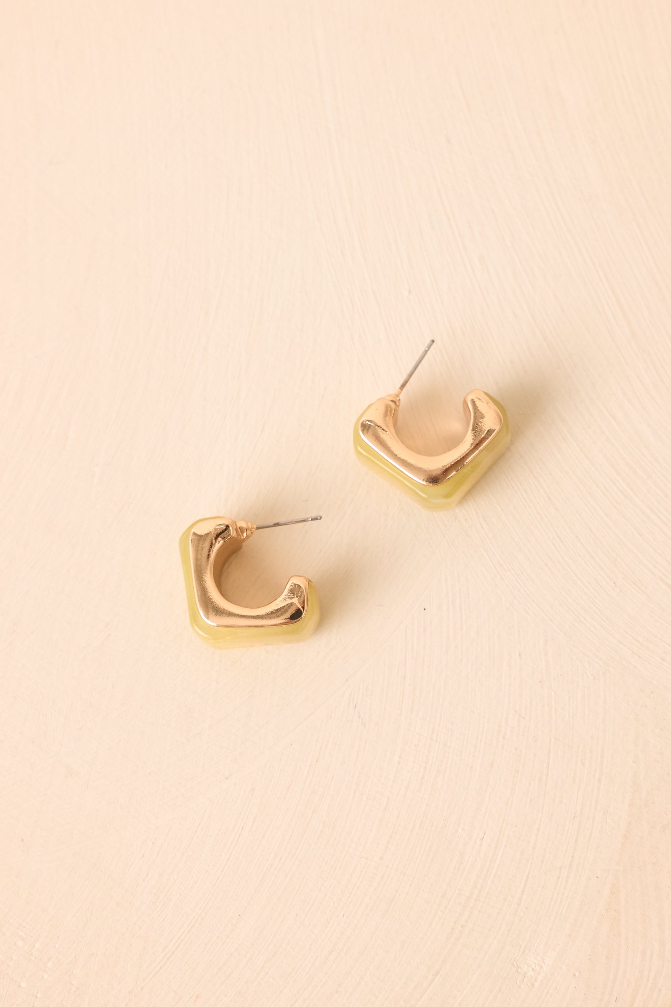Golden and chartreuse square hoop earrings displayed against a neutral beige background, highlighting their contemporary shape and glossy finish.