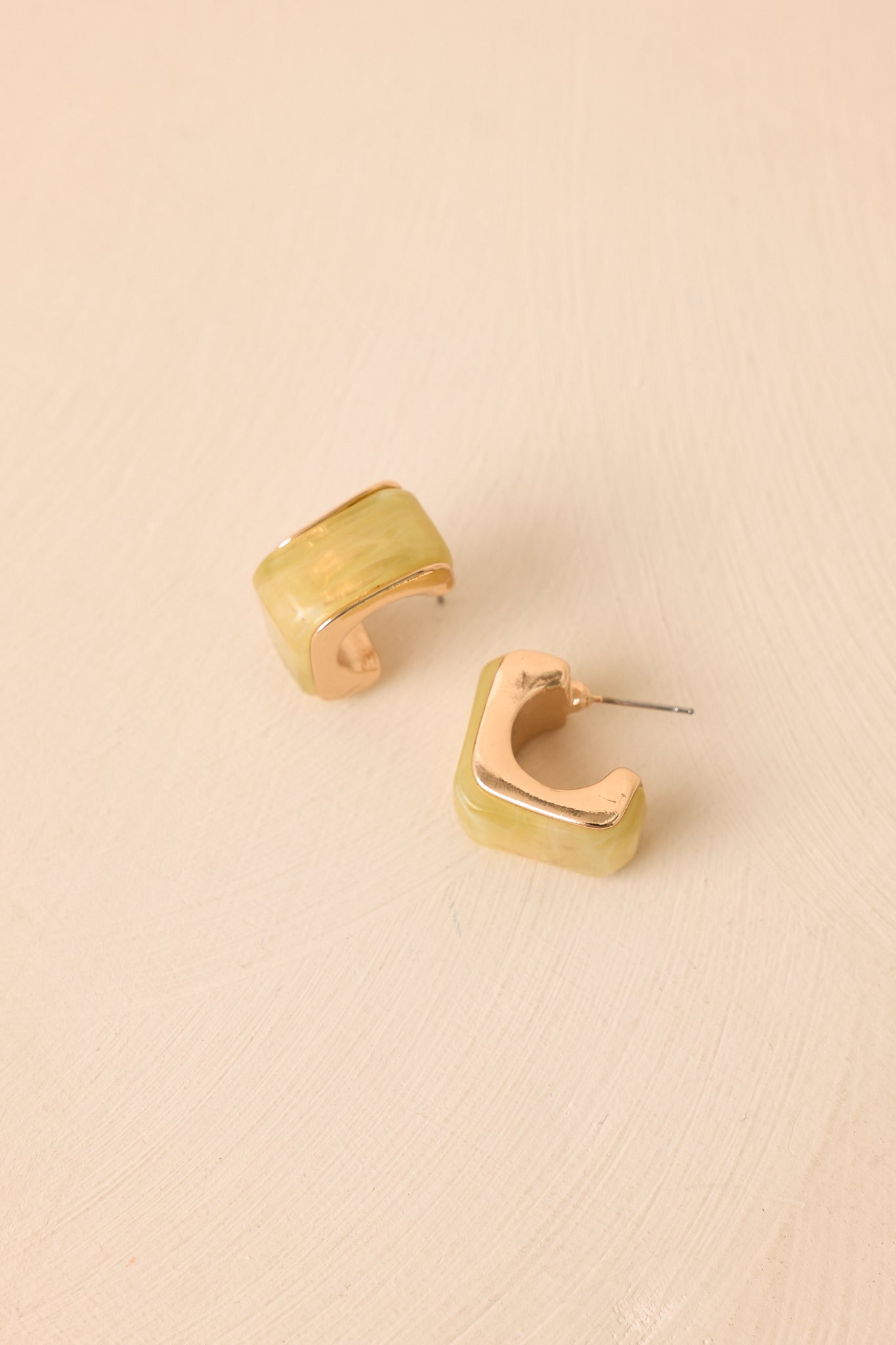 Modern geometric hoop earrings featuring chartreuse resin and polished gold-tone metal, styled on a beige background for a clean, elevated look.