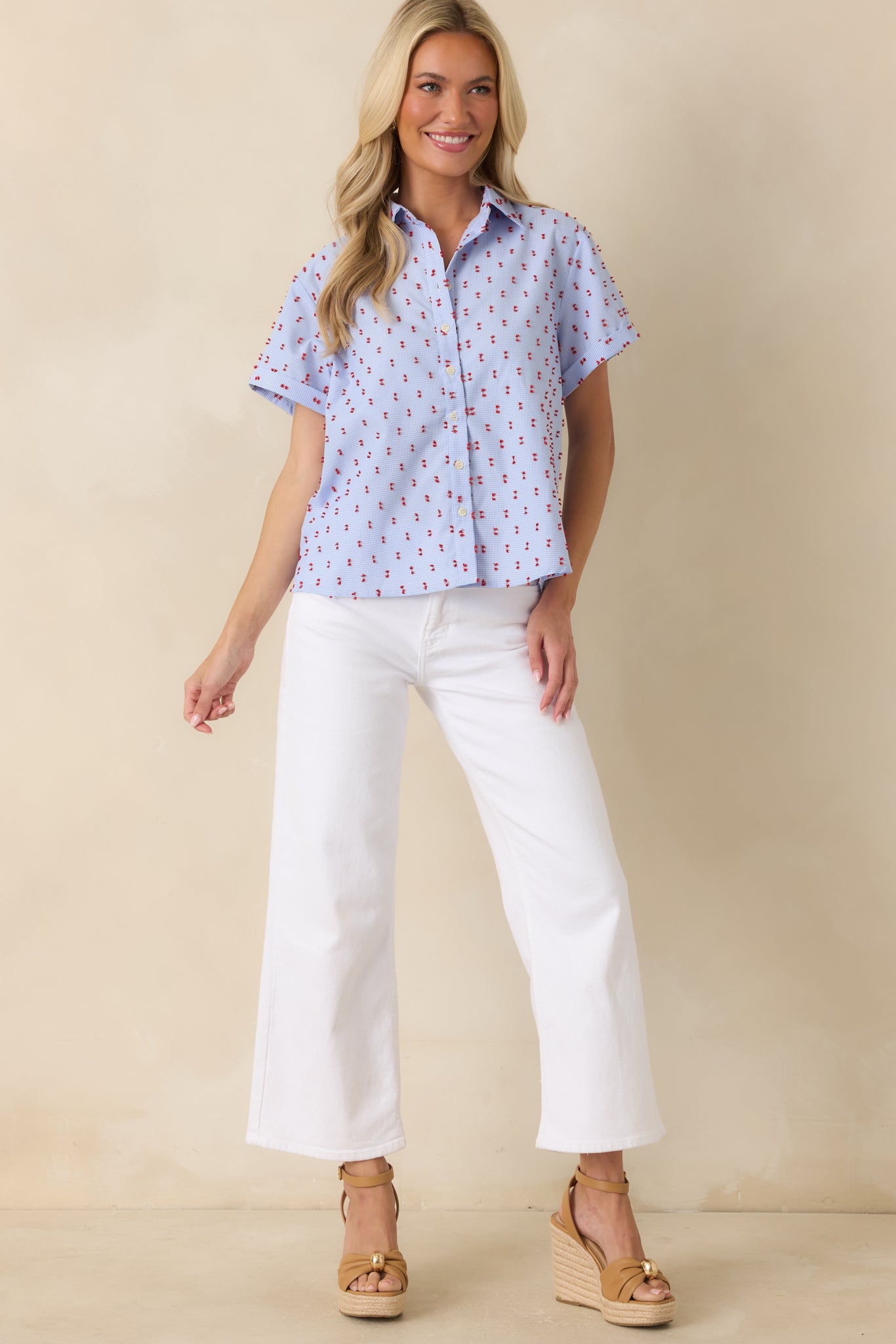 Blue gingham button-front top featuring a relaxed silhouette, short sleeves, and contrasting red tufted embroidery throughout the checkered fabric.
