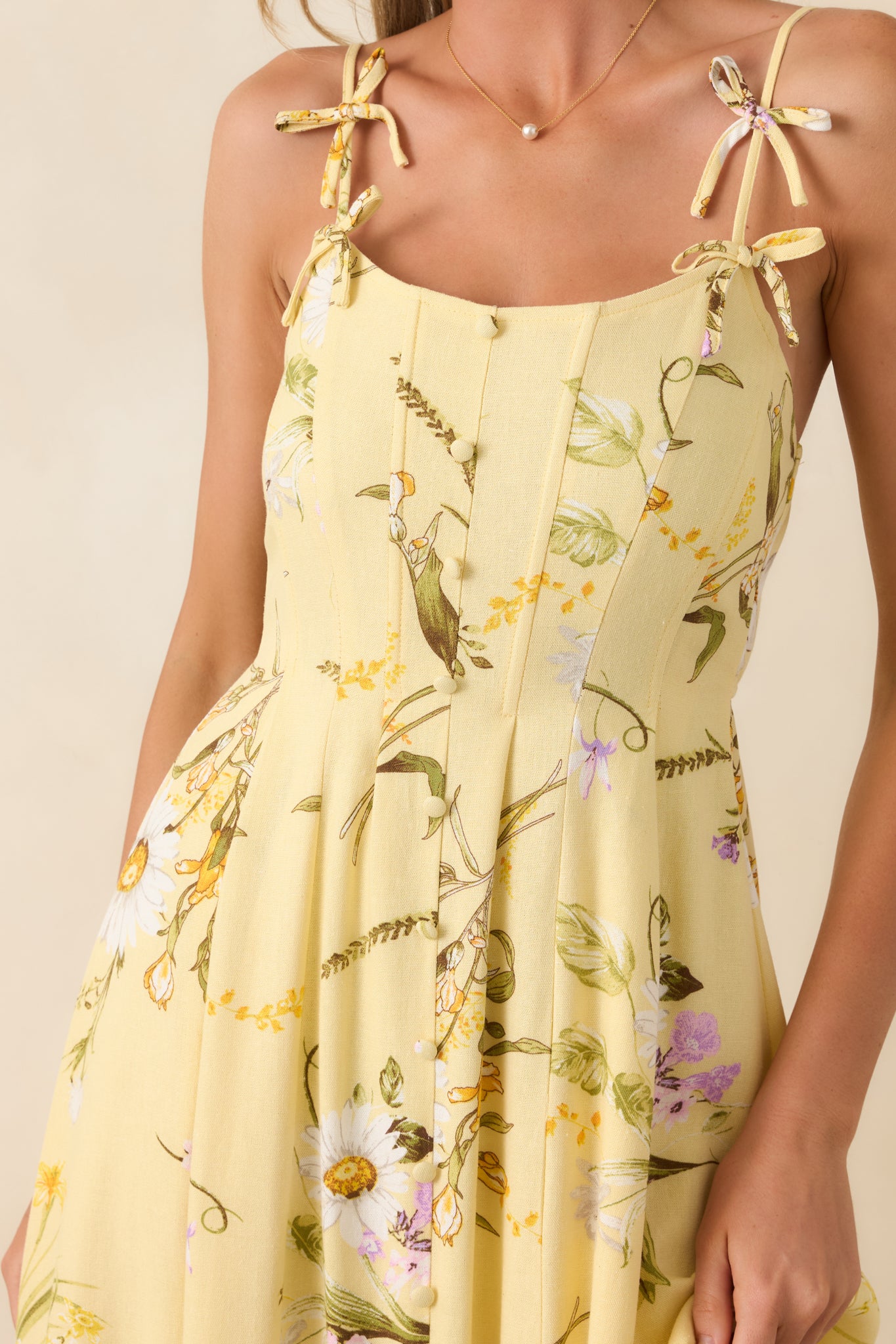 Detailed view of yellow floral print with button-front bodice, textured linen-blend fabric, and adjustable bow-tie strap accents.
