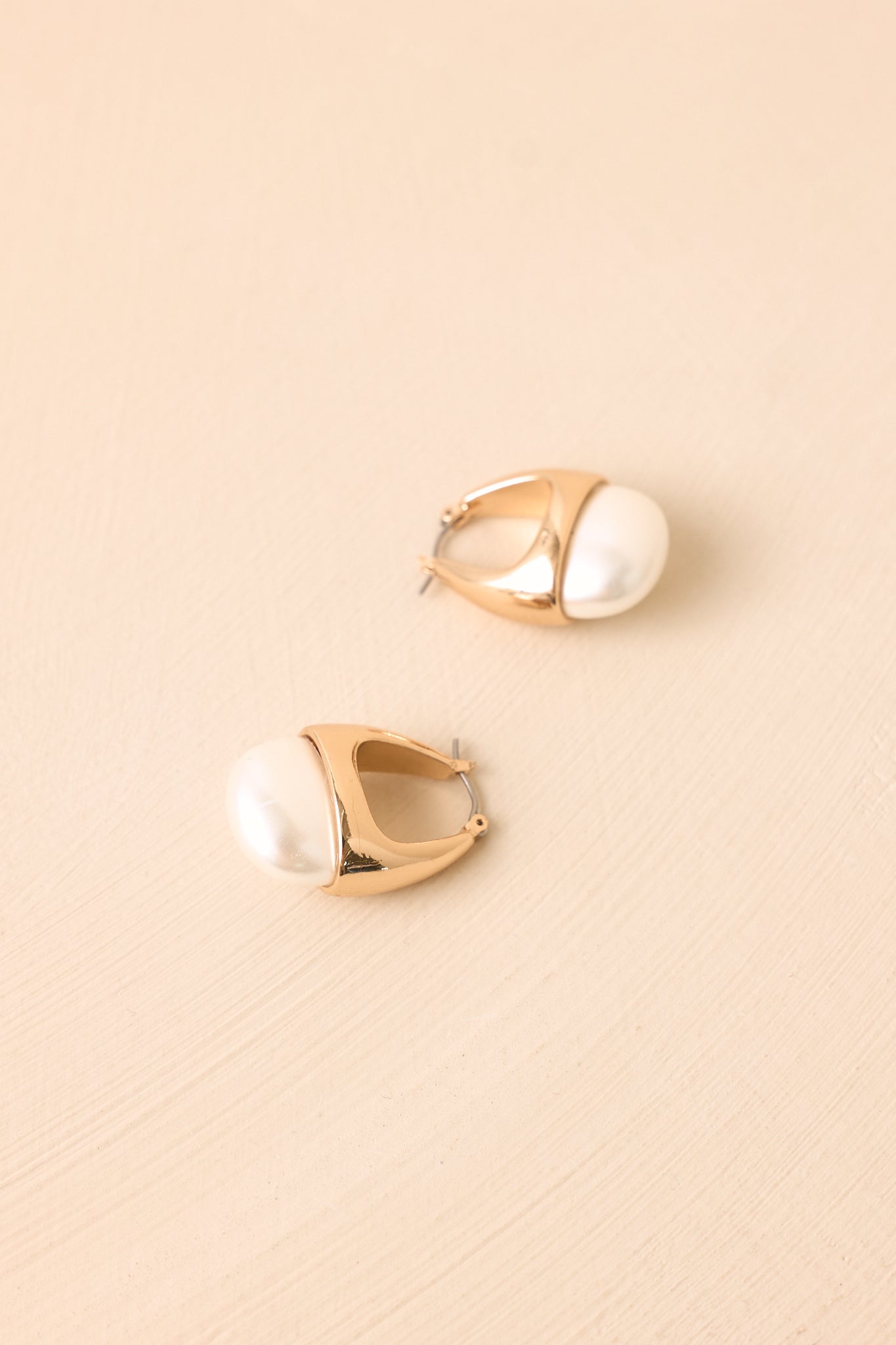 Gold-tone pearl hoops showcasing the rounded silhouette, polished metallic finish, and secure latch back closures.