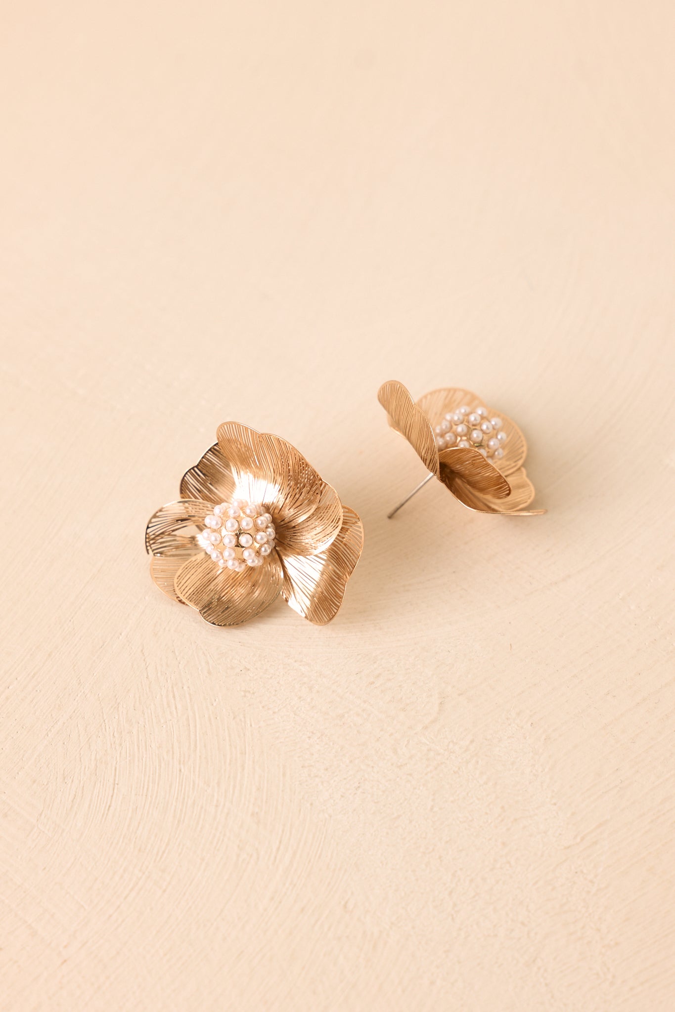 Gold statement studs showcasing a dimensional flower design with polished metallic petals and delicate bead accents.