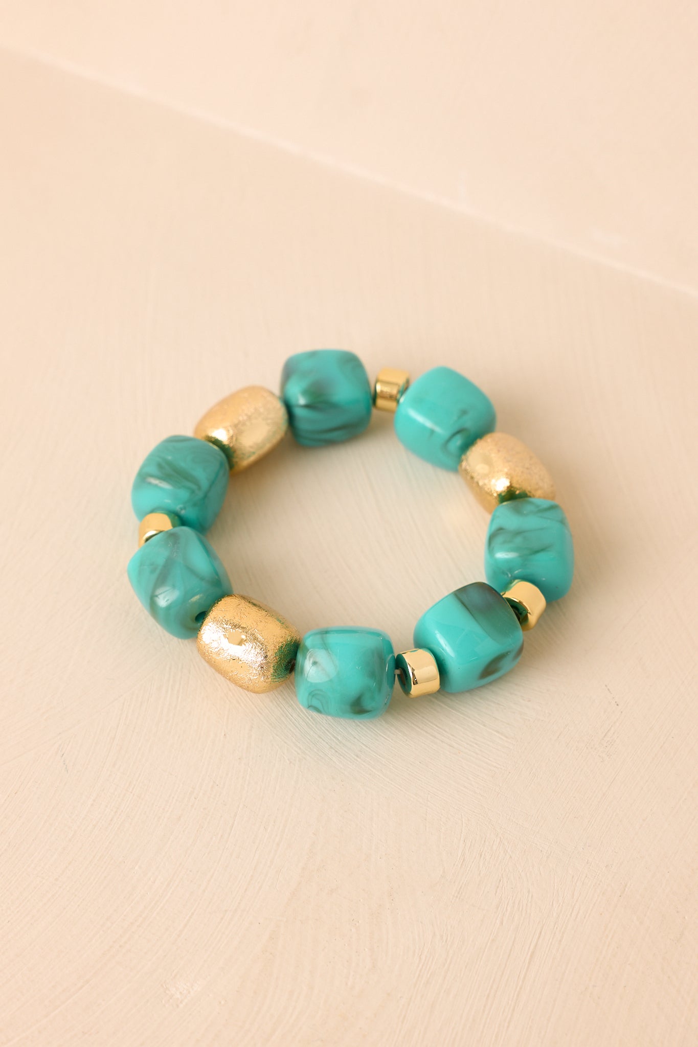 Turquoise and gold bracelet displayed on a beige background, featuring rounded beads and dimensional metallic detailing.