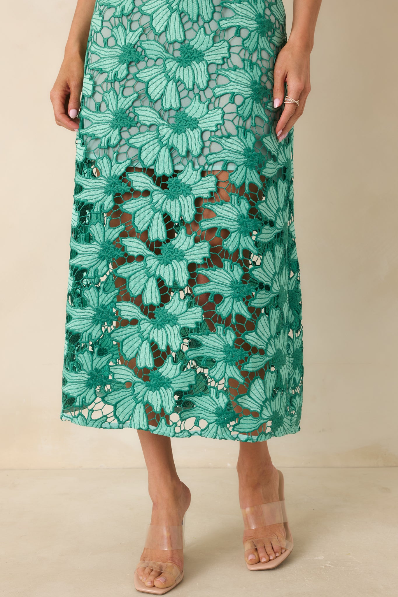 Intricate floral lace overlay texture on green midi dress fabric.