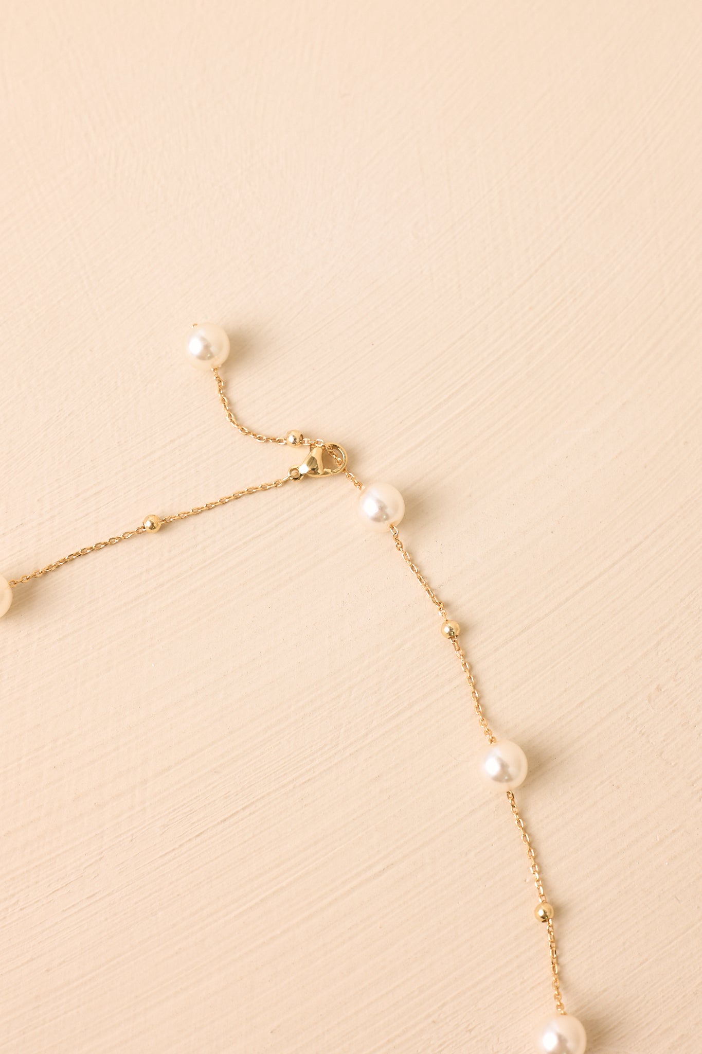 Gold pearl chain necklace displayed on a beige background, featuring evenly spaced pearls and a refined clasp closure.