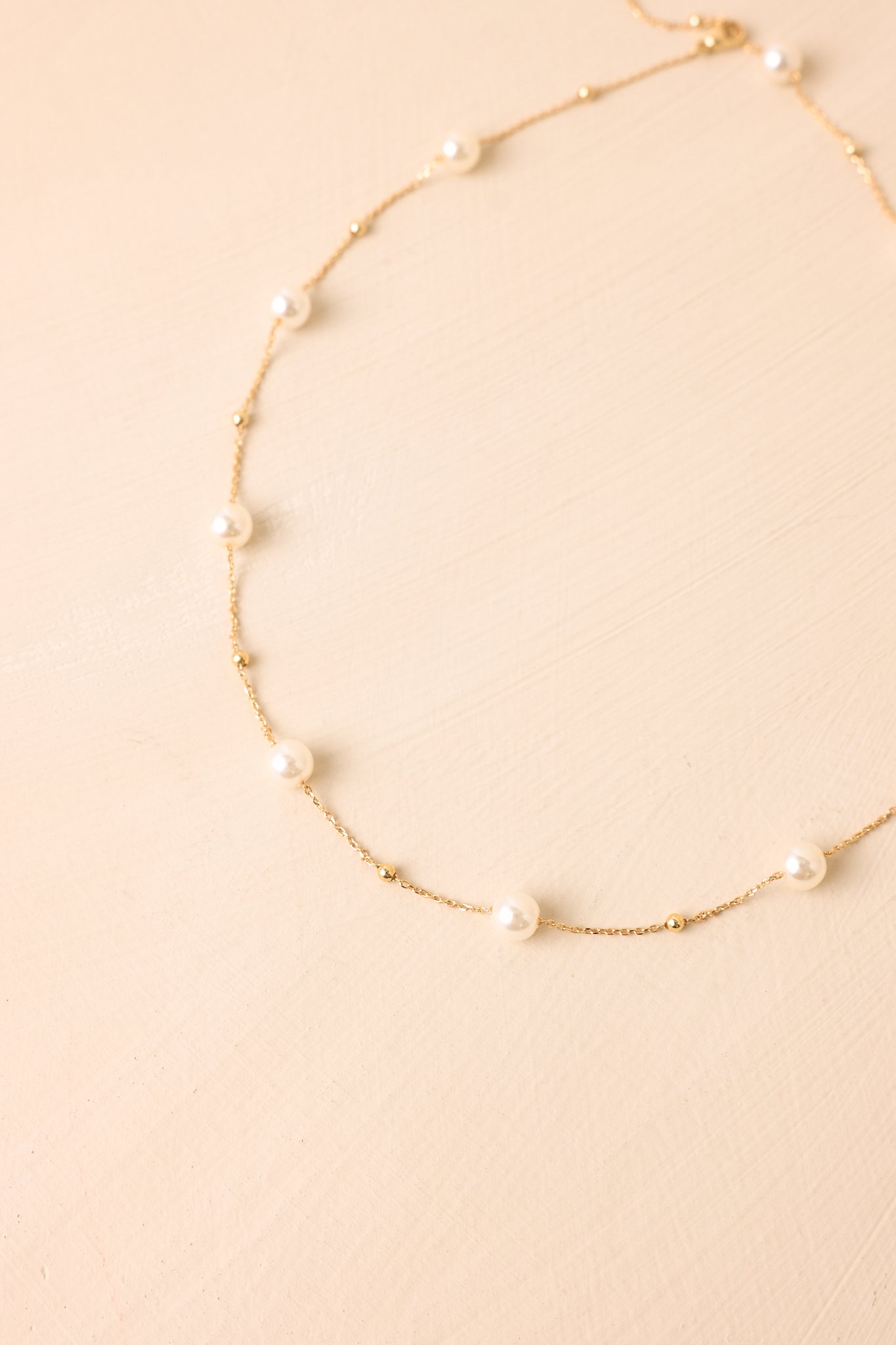Close-up of the necklace highlighting the smooth faux pearl details, fine gold-tone chain, and delicate construction.