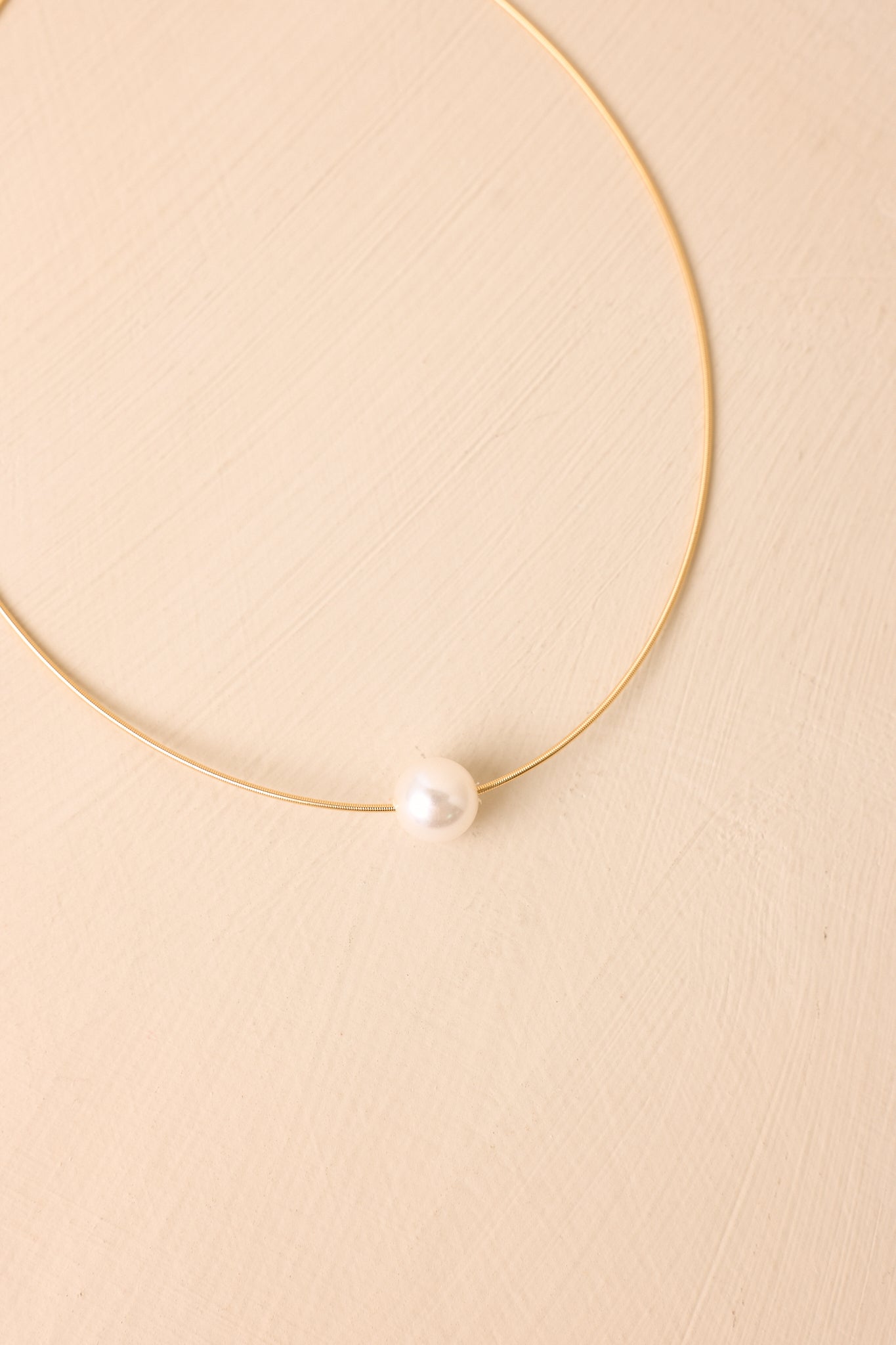 Delicate pearl necklace displayed on a beige background, featuring a polished gold-tone chain and refined pendant design.