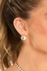 Close-up of model wearing gold earrings that feature square rhinestone studs. 
