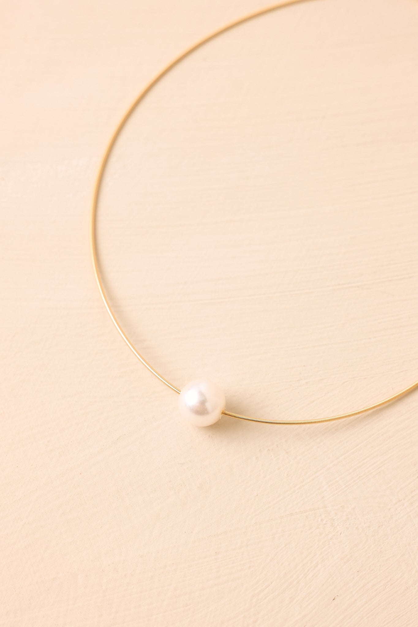 Close-up of the necklace highlighting the glowing pearl pendant and smooth gold-tone snake chain texture.