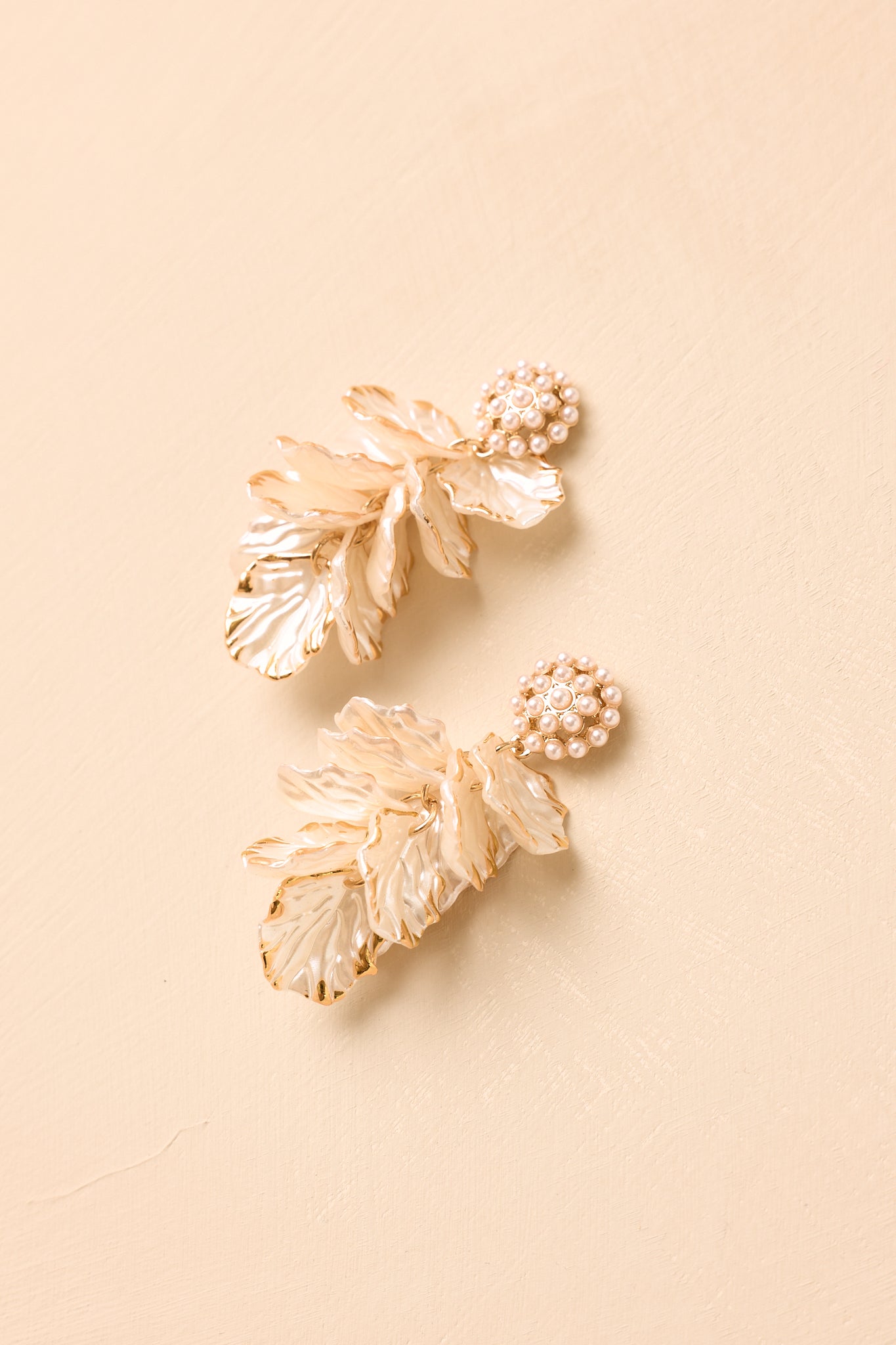 Statement gold earrings showcasing sculpted ivory petal accents, pearl detailing, and a refined layered silhouette.