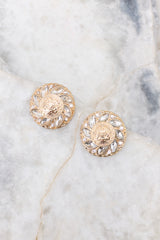 Overhead close up view of earrings that feature a gold textured stud with rhinestone detailing, and a secure post backing.