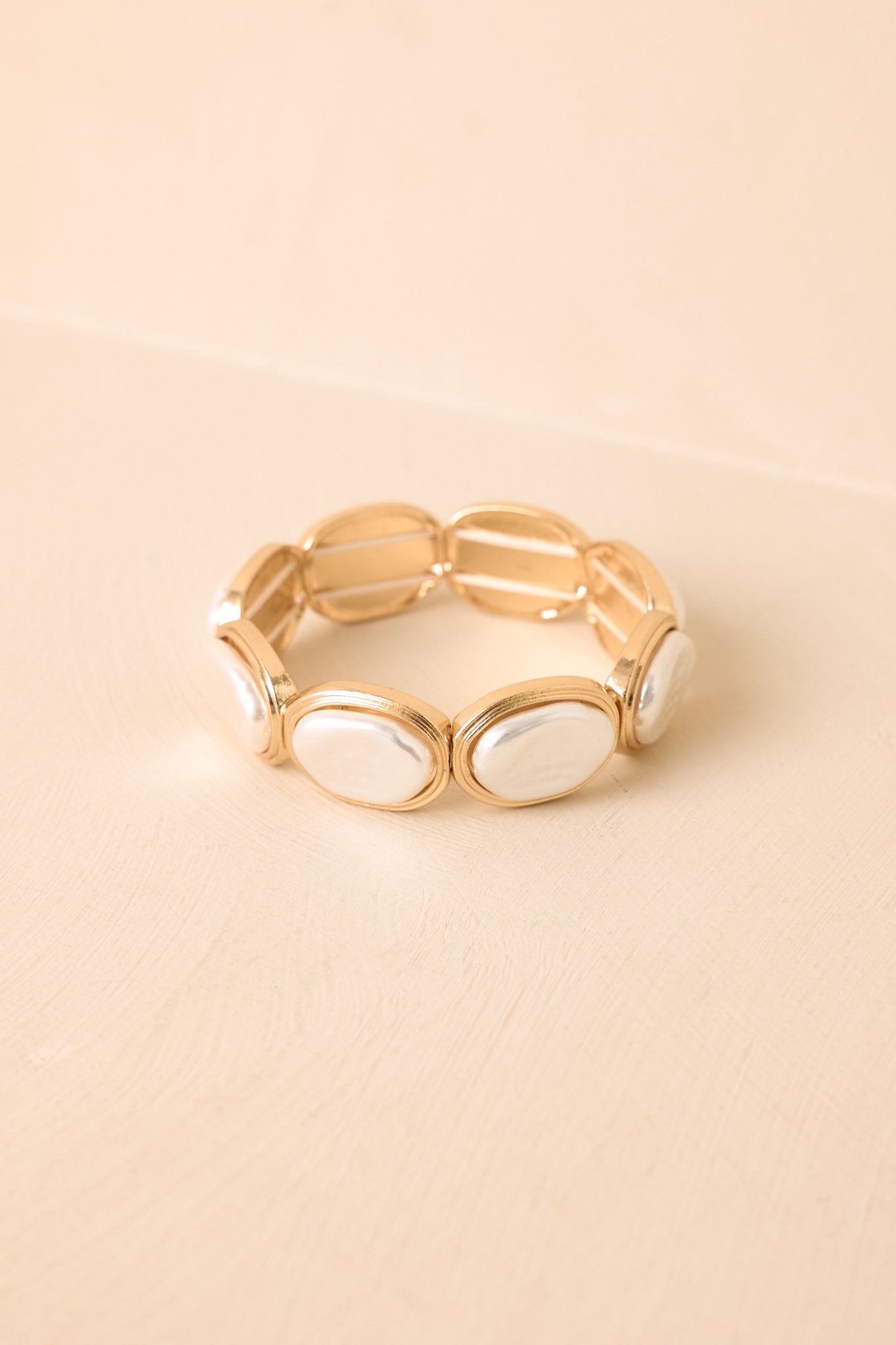 Gold and pearlescent stretch bracelet displayed on a beige background, featuring oval accents and refined metallic frames.