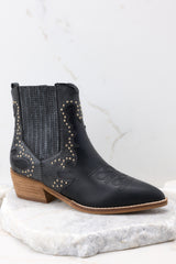 These black ankle boots feature a pointed toe, a side zipper closure, a stretchy side panel, embroidered detailing, and a stacked heel.