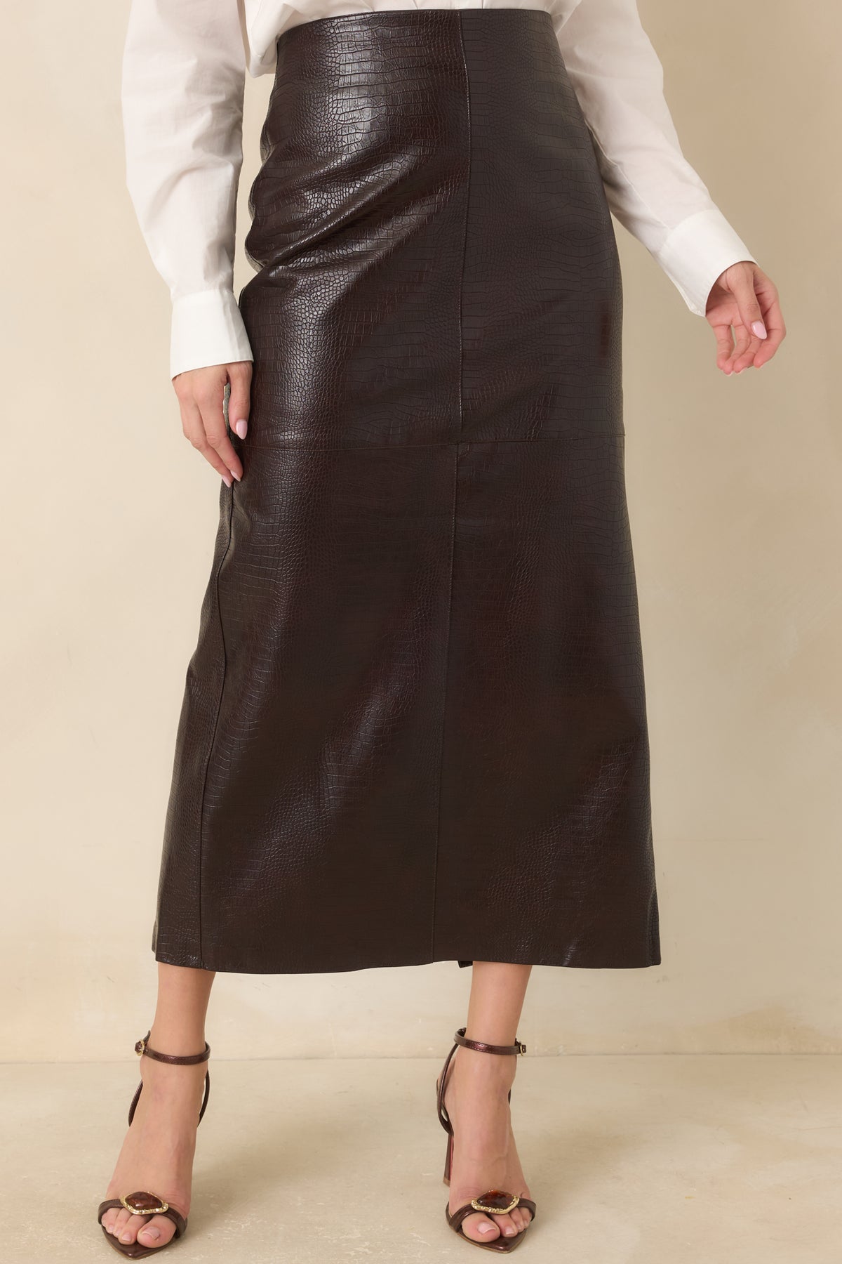 The espresso skirt showcases its high-rise waistband and glossy crocodile-textured faux leather finish.