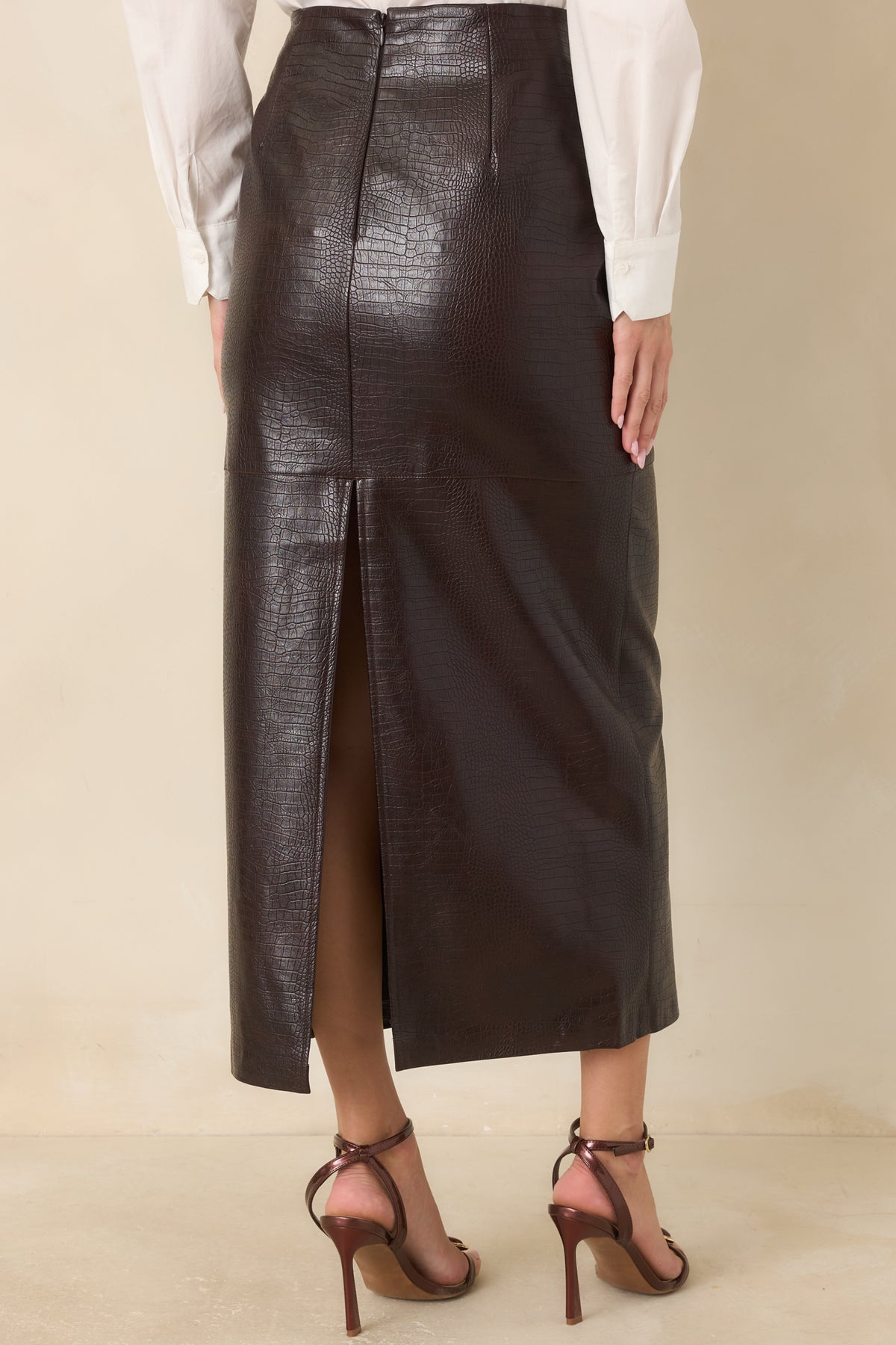 Rear view of the espresso crocodile-textured midi skirt featuring a concealed zipper, clean panel seams, and a back slit.