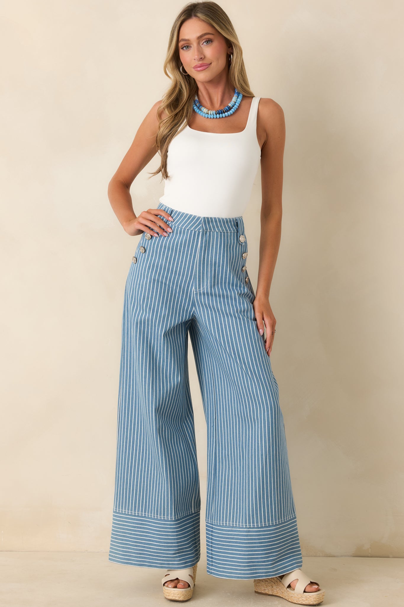 Blue striped wide leg pants featuring a high-rise waist, sailor-inspired silver button detailing, and a relaxed flowing leg shape.