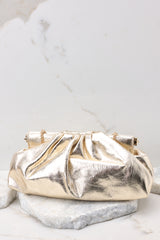 Close up view of this bag that features a wide hinged opening that snaps shut (no zipper or snap button closure) , a non-removable gold chain strap, and one zipper pocket inside.