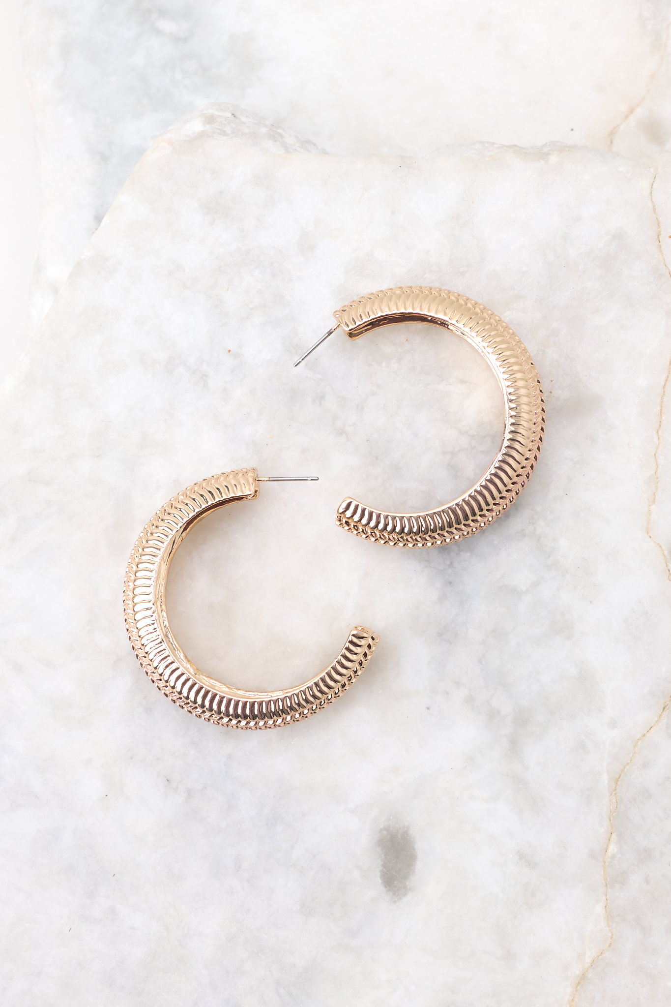 Overhead close view of earrings that feature a gold textured finish, a wide hoop design, and secure post-back fastening.