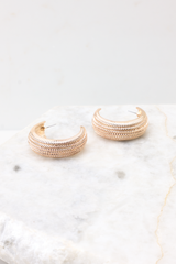 Side detailed view of earrings that feature a gold textured finish, a wide hoop design, and secure post-back fastening.
