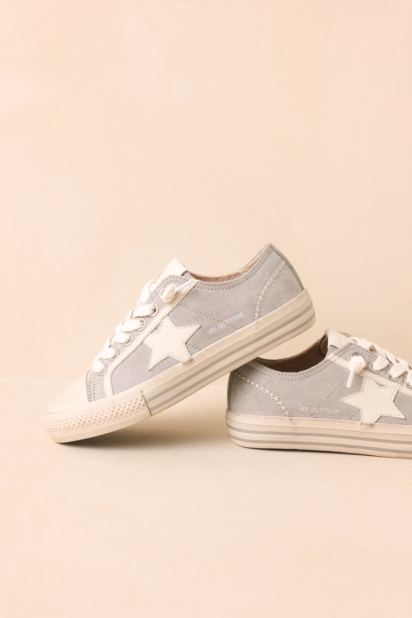 Low-top dusty blue suede sneakers highlighting the classic star detail, flexible rubber outsole, perforated side panels, and soft suede construction against a neutral beige backdrop.