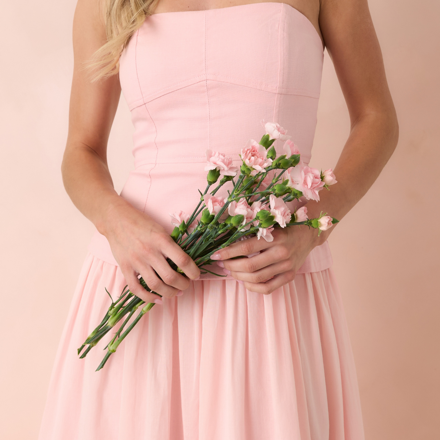 Person wearing a pink dress holding pink flowers against a light pink background
