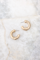 Close up view of these earrings that feature a textured design, worn gold finish, and secure post-back fastenings. 