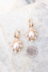 These earrings feature gold hoops, oval pearl dangles with smaller pearl and gold detailing, and a secure post backing compared to a quarter for actual size. 